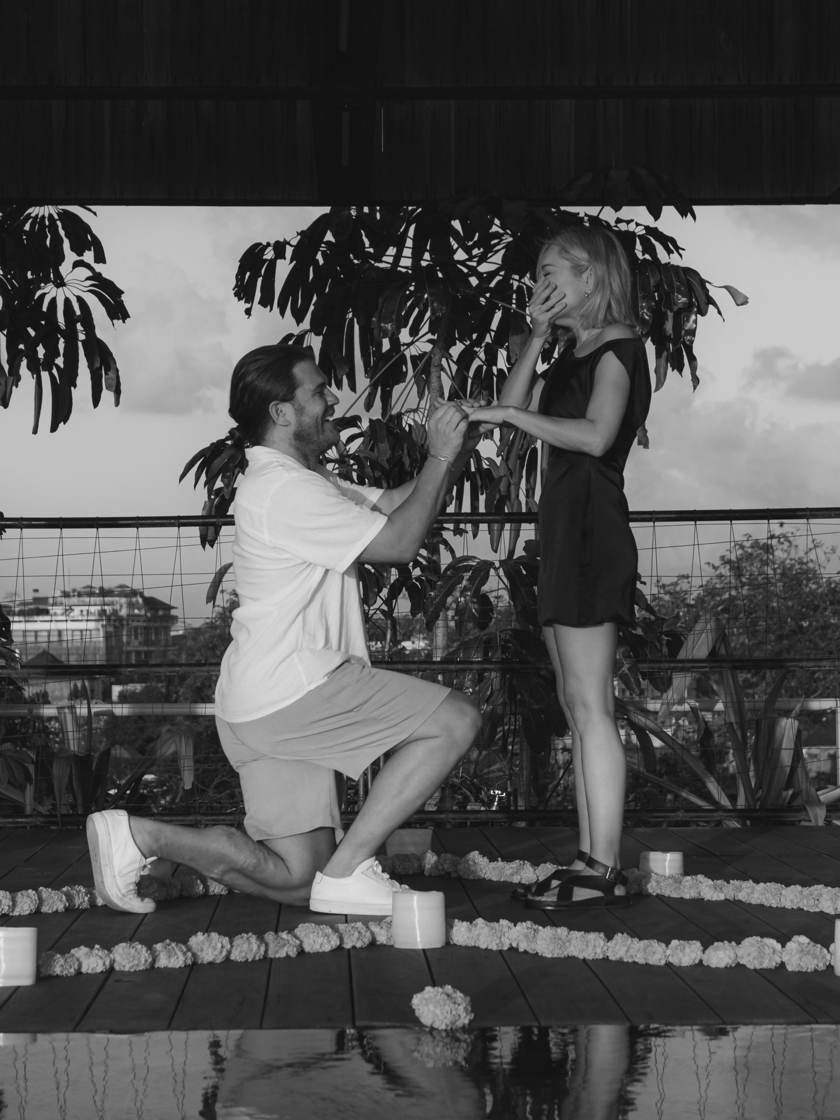 Man proposing to a surprised woman on a decorated terrace. Captures romance, luxury jewellery, engagement. Elegant outdoor setting. Black and white.