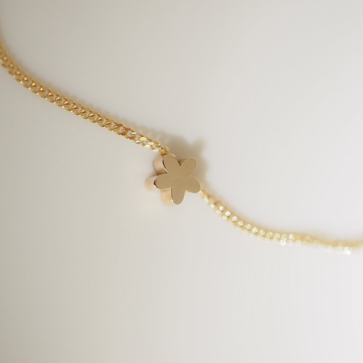 Gold necklace with a delicate flower-shaped pendant on a textured chain, set against a soft, neutral background.