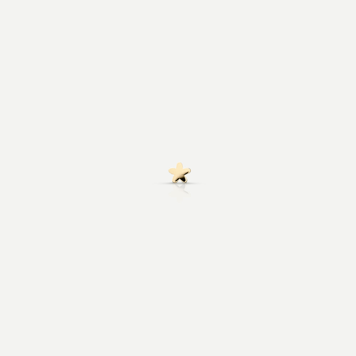Gold star-shaped stud earring on a light background; luxury jewellery minimalism.