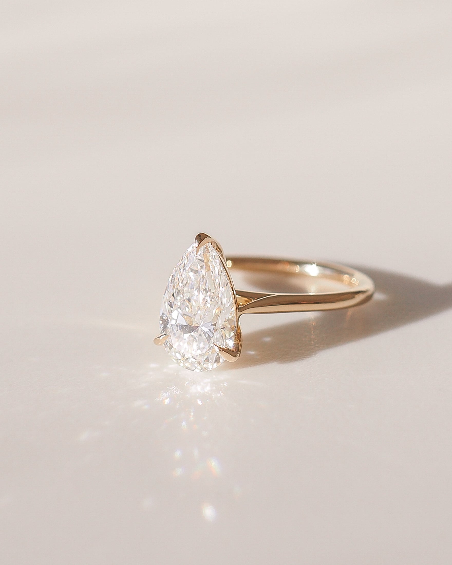 A pear-shaped diamond gold engagement ring glistens in soft light on a smooth surface, showcasing luxury jewellery appeal.