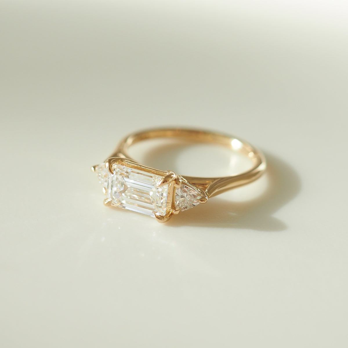 Gold three-stone engagement ring with emerald-cut center diamond and side triangles