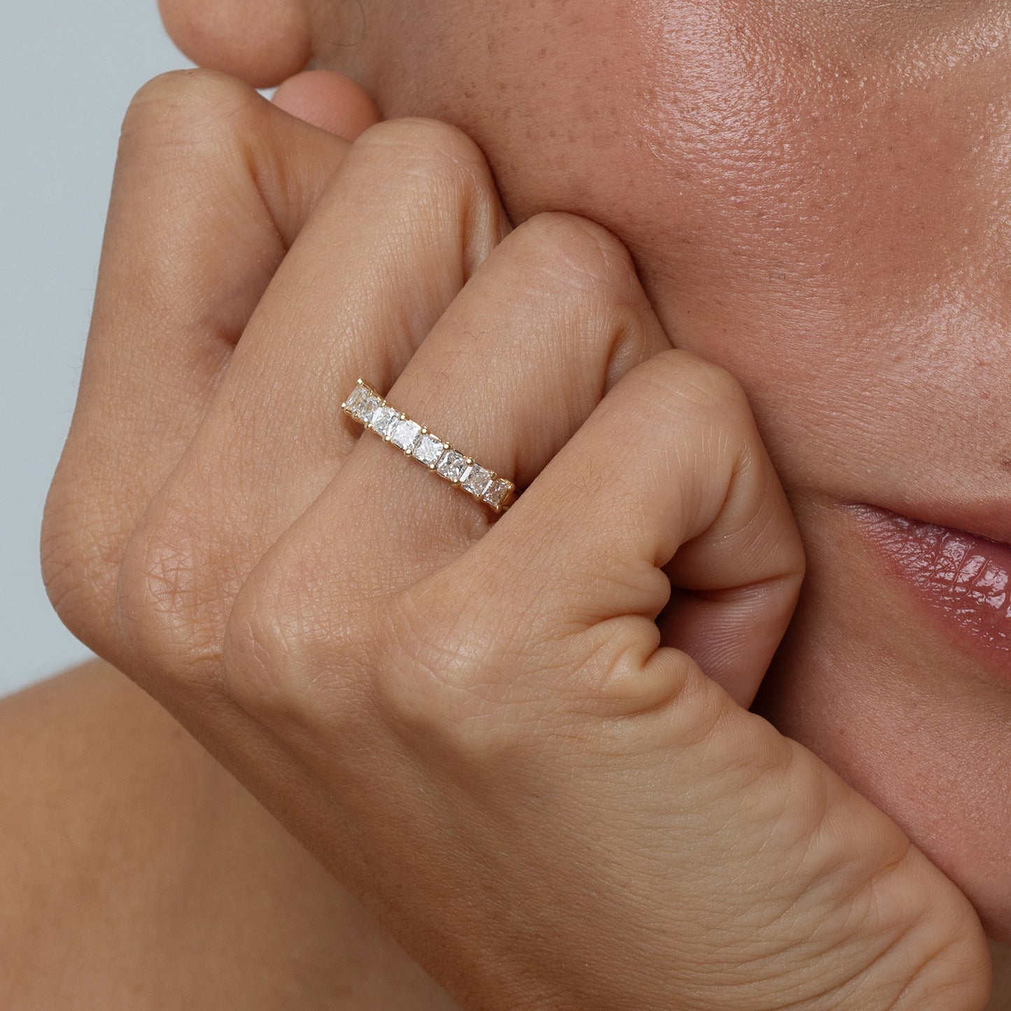 Close-up of a hand wearing a diamond ring on a neutral background