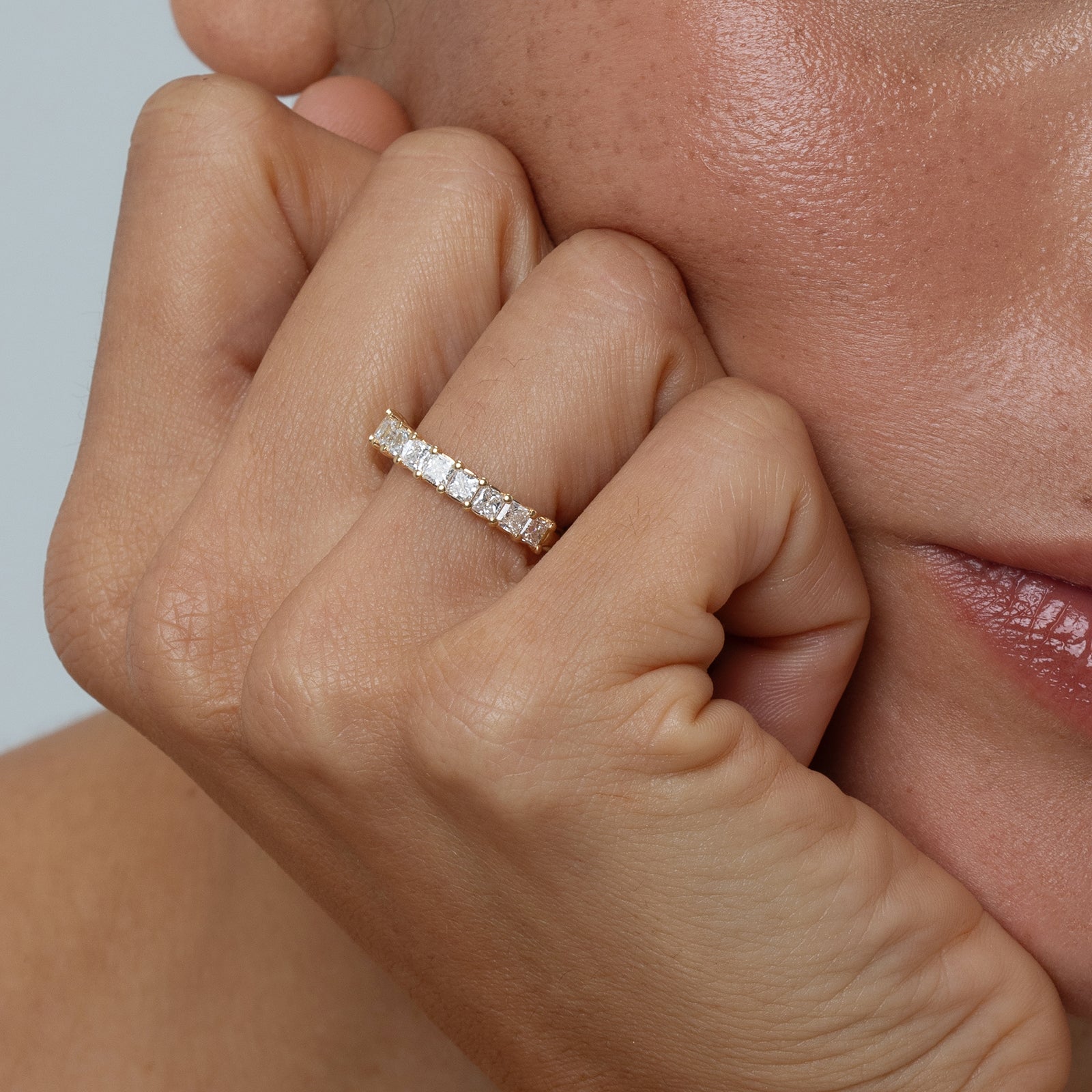 Close-up of a hand wearing a diamond ring on a neutral background