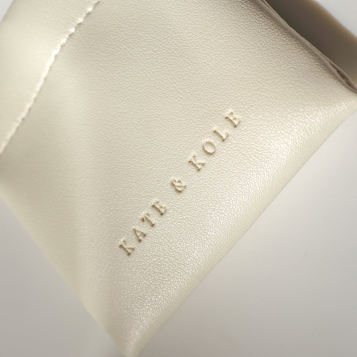 Cream leather jewellery pouch with embossed "KATE & KOLE" branding, showcasing luxury design and elegance.