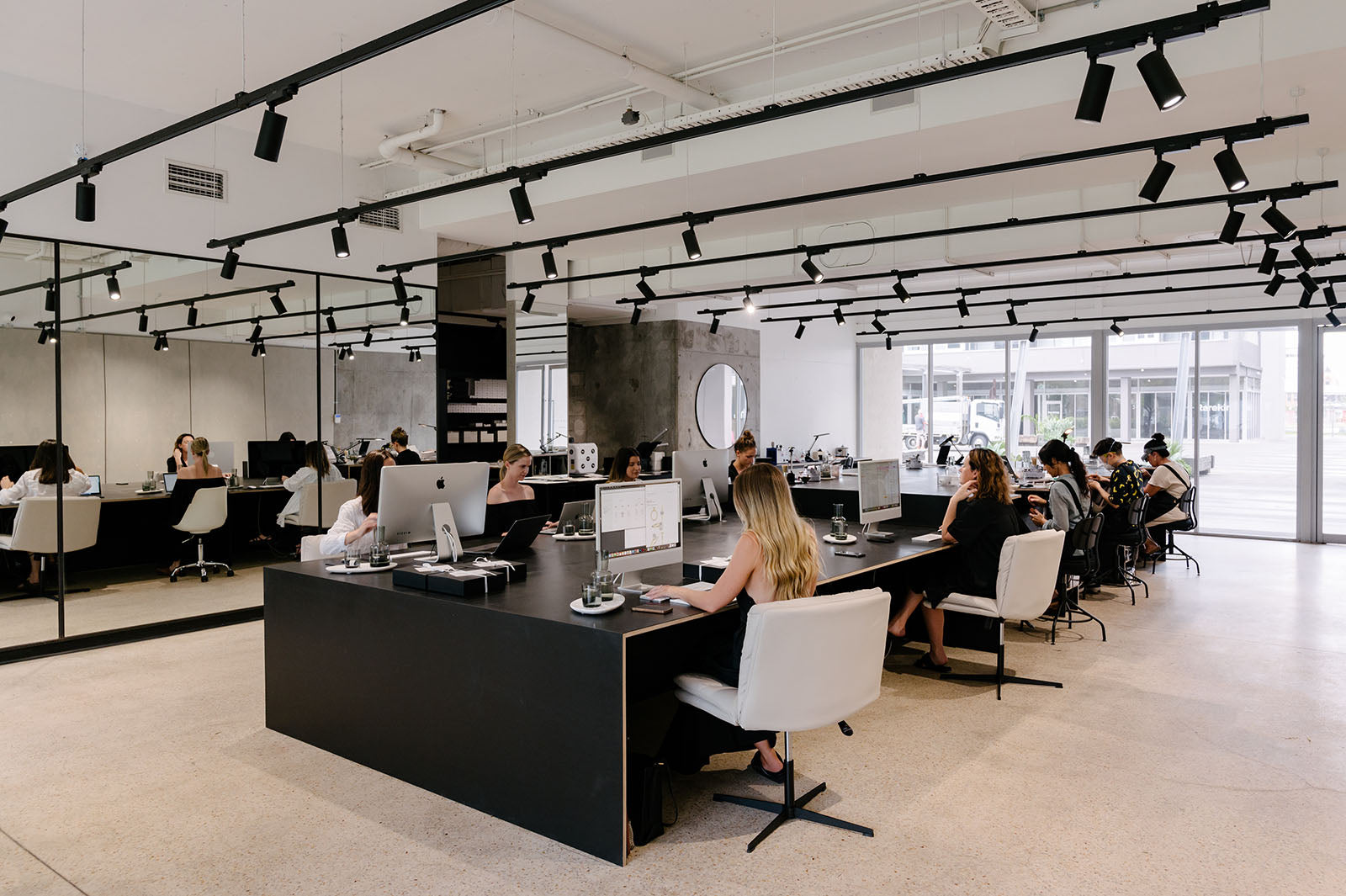 Modern jewellery showroom with sleek black desks, white chairs, and mirrored walls. Customers consult with staff in elegant, minimalist space.