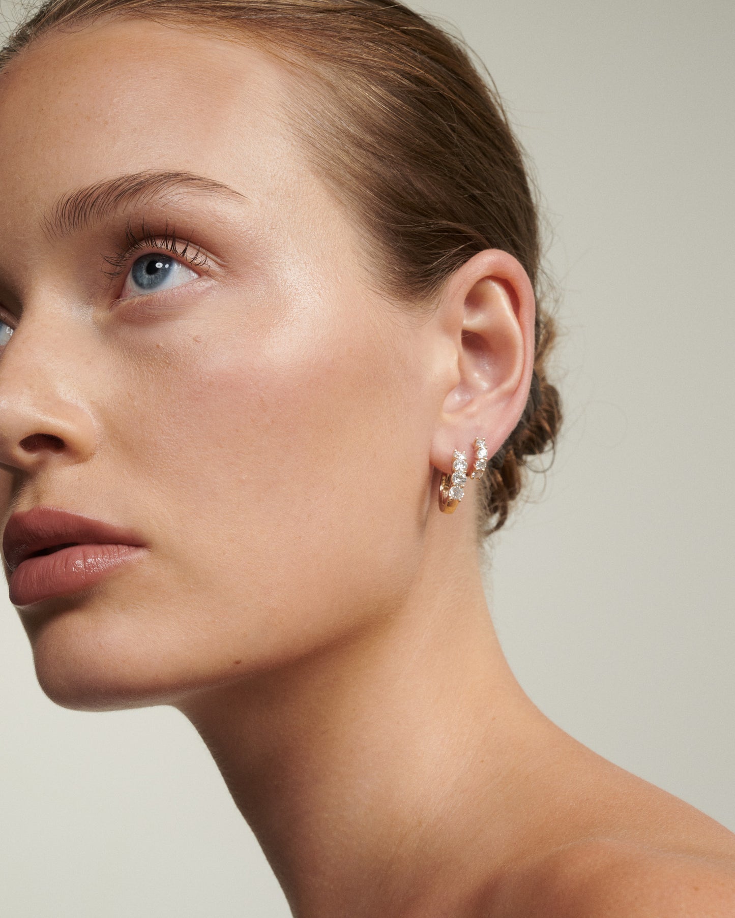 Close-up of a woman wearing a diamond earring against a neutral background