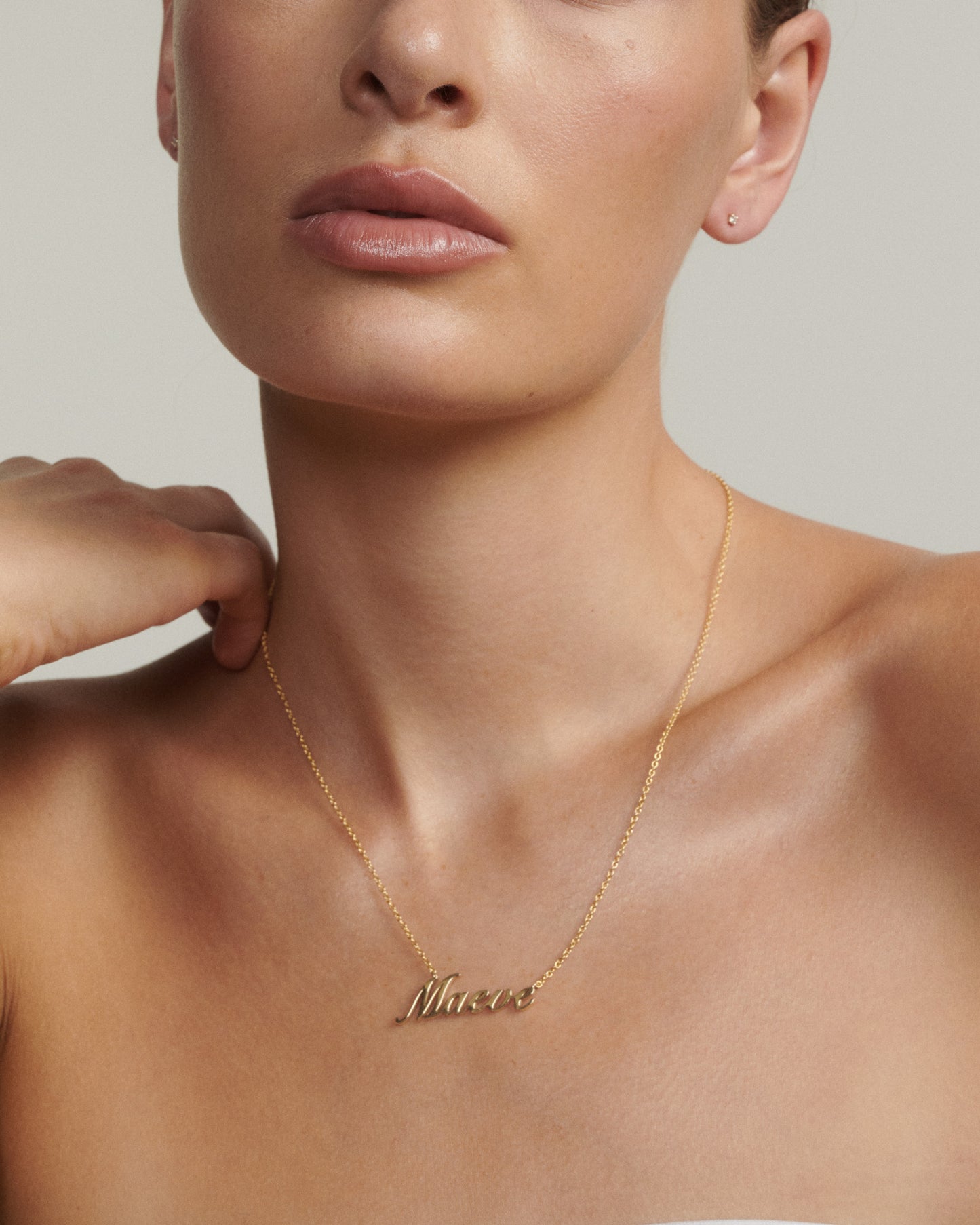 Gold necklace with a name pendant worn by a person against a neutral background