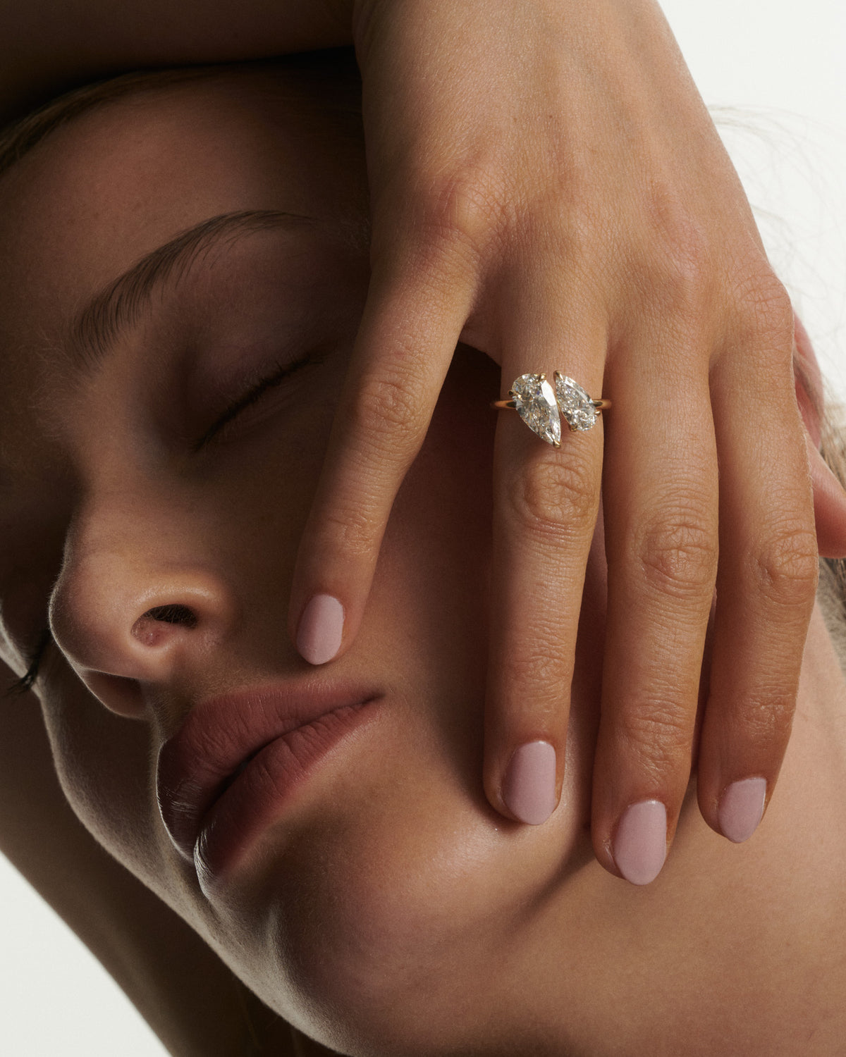 Close-up of a woman's face with a hand resting on her cheek, wearing a diamond ring.