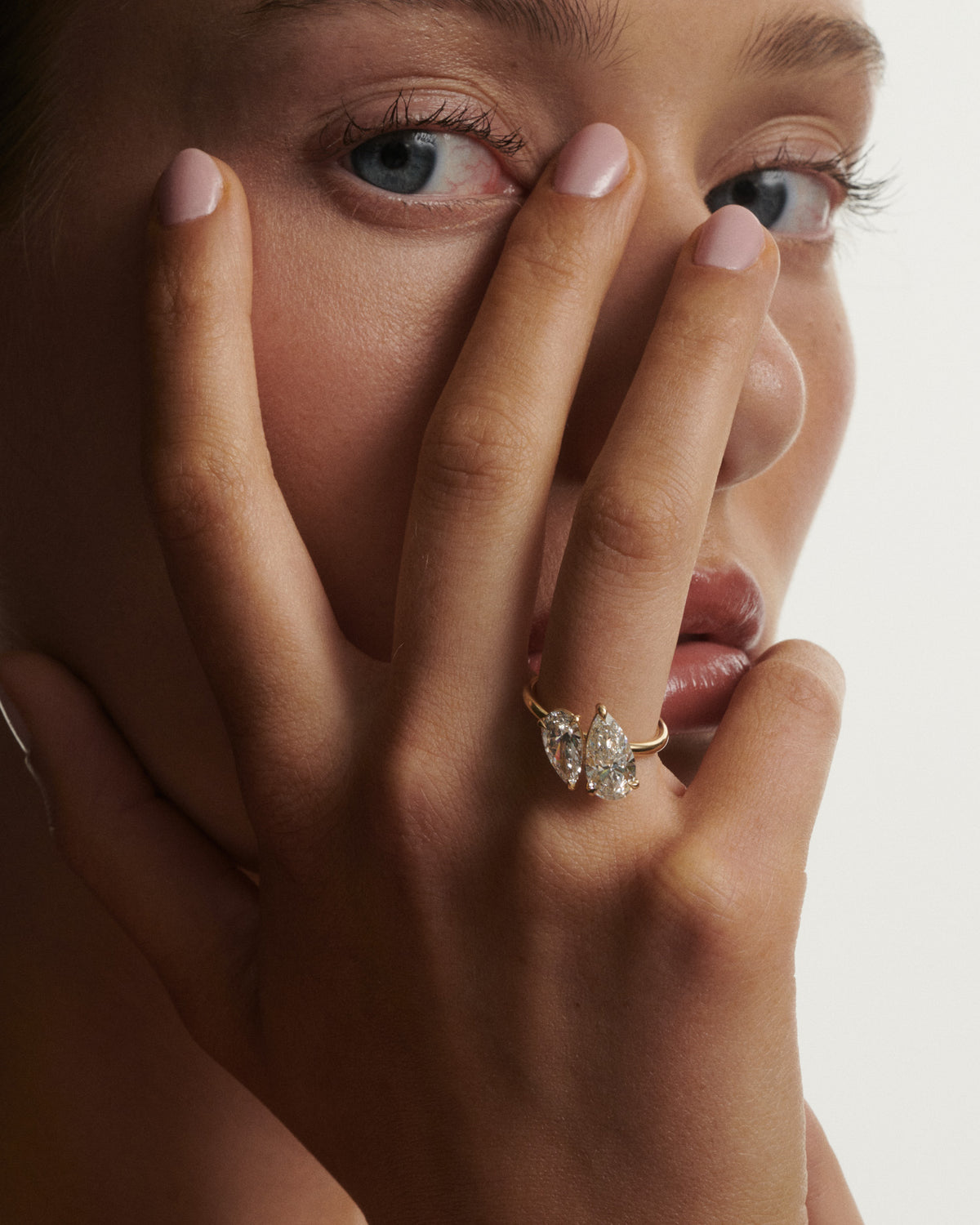 Close-up of a hand with a diamond ring on a neutral background