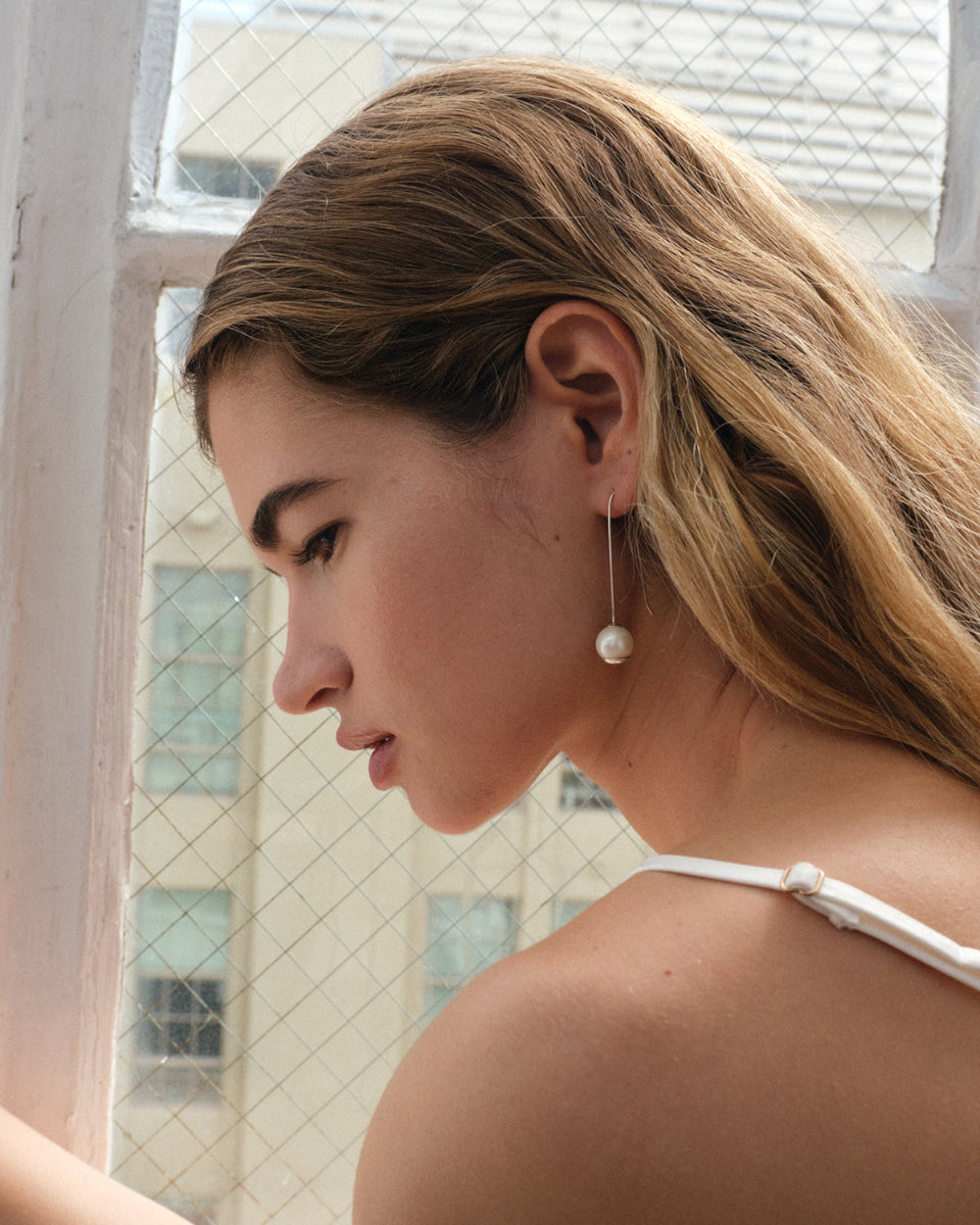 Woman wearing a pearl earring in front of a window with tiled walls.