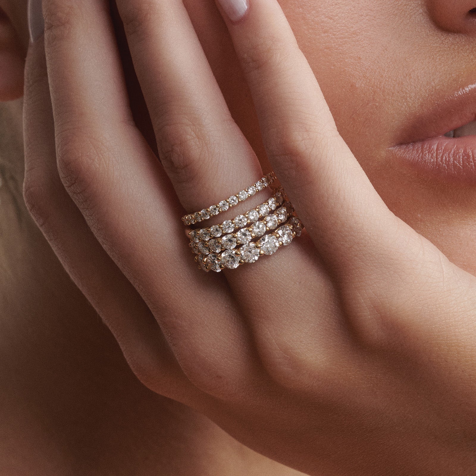 Close-up of a hand wearing four Arraya diamond rings on a neutral background