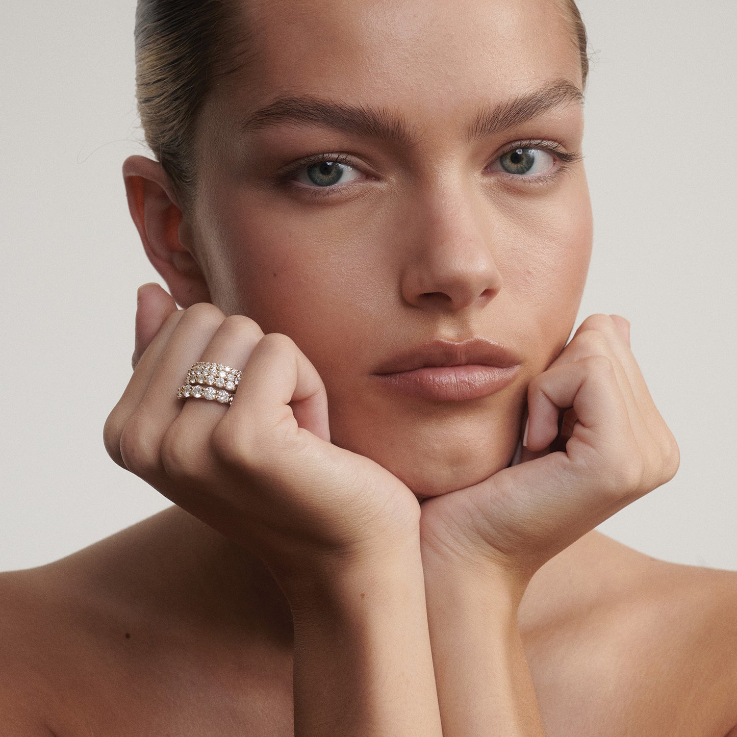 Woman with hands under chin wearing a ring on a neutral background