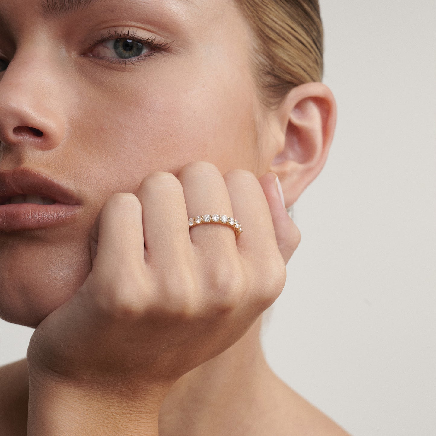Close-up of a woman's hand with a diamond ring on a neutral background