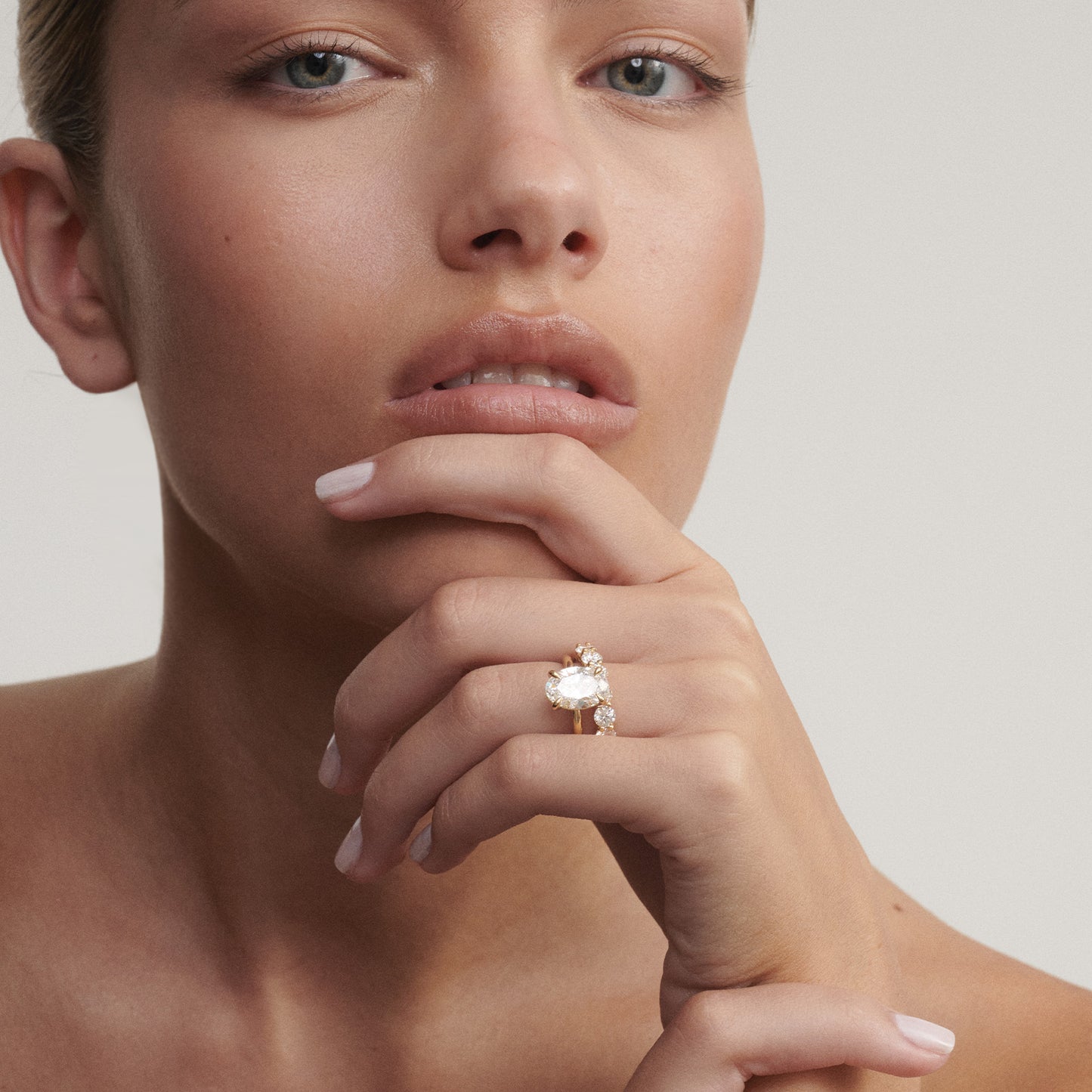 Close-up of a woman's hand wearing a diamond ring on a neutral background