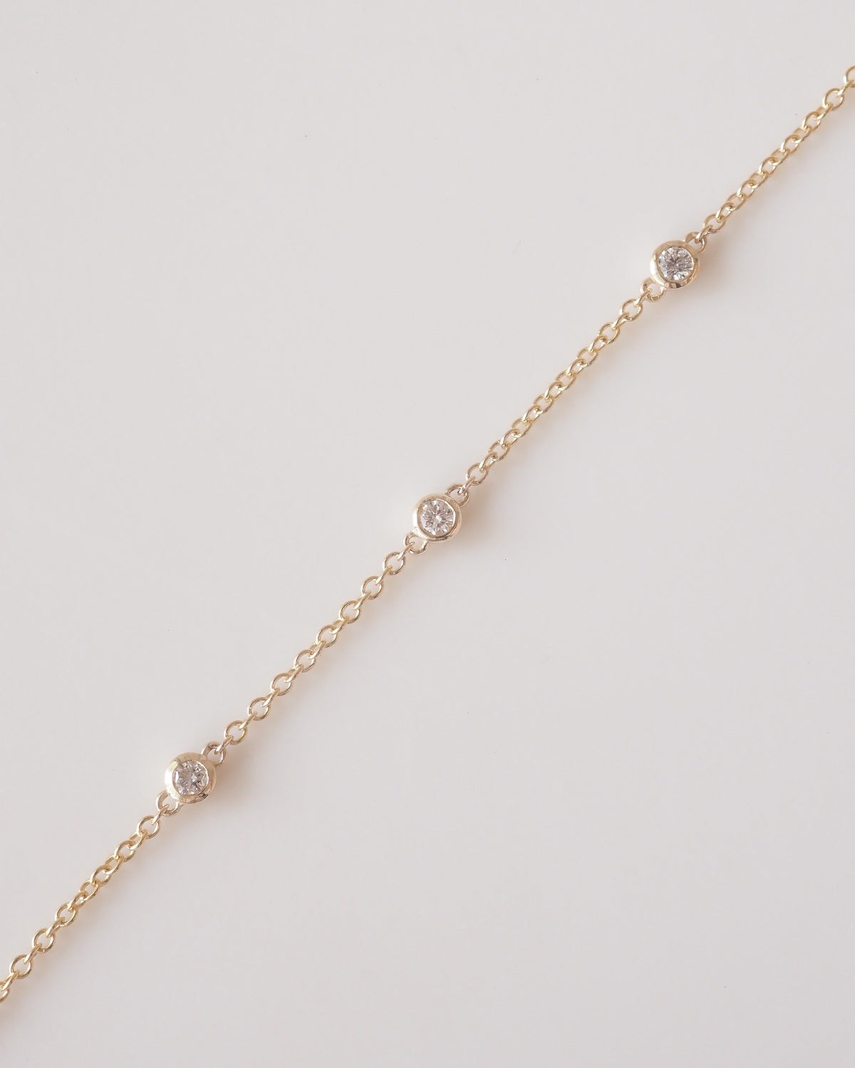 A delicate gold chain bracelet with three small round bezel-set clear stones spaced along the length of the chain, photographed on a clean off-white background.