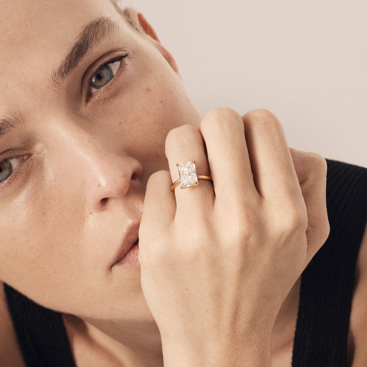 Close-up of a woman's face wearing a gold ring with a diamond on a neutral background