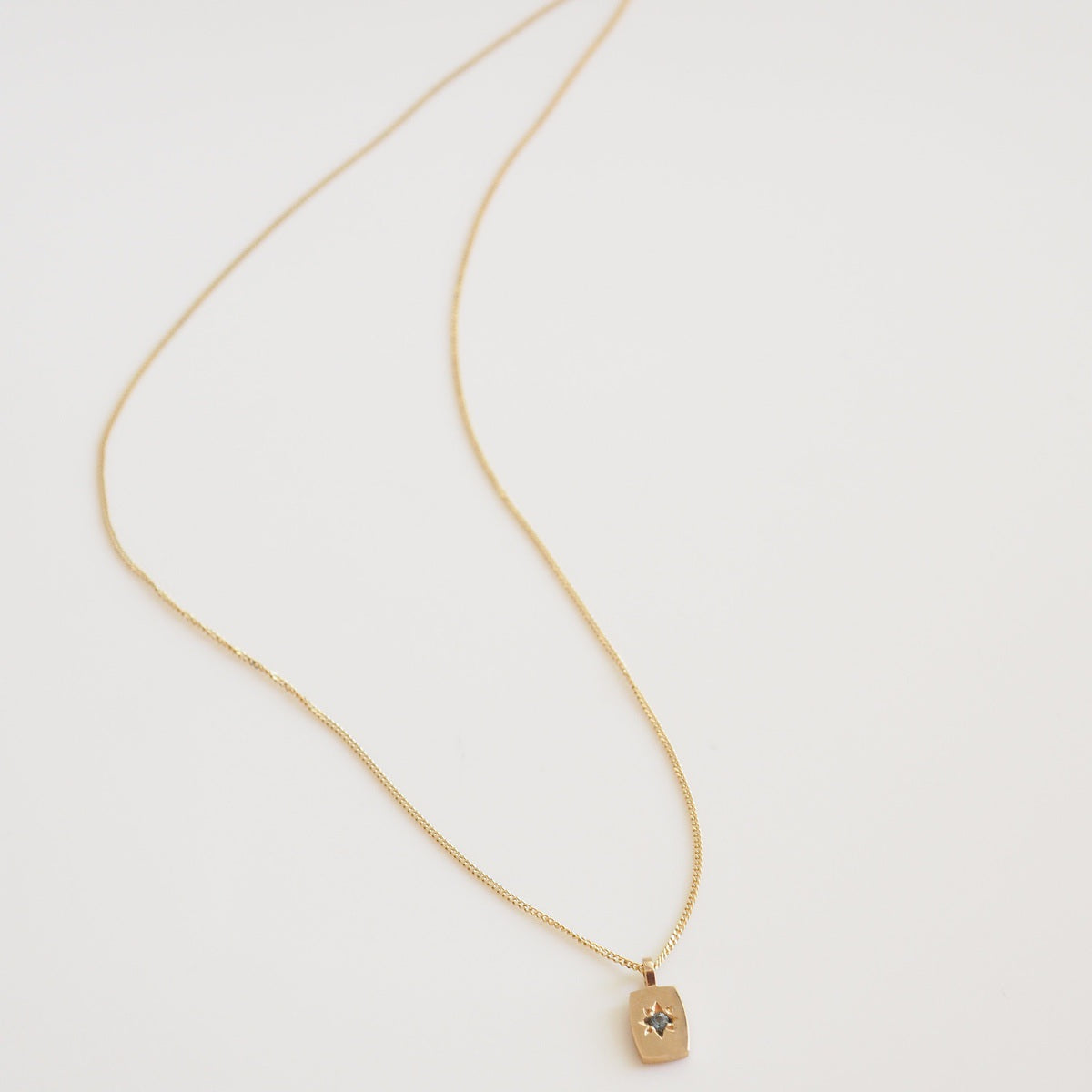 Gold necklace with a small pendant on a light gray background