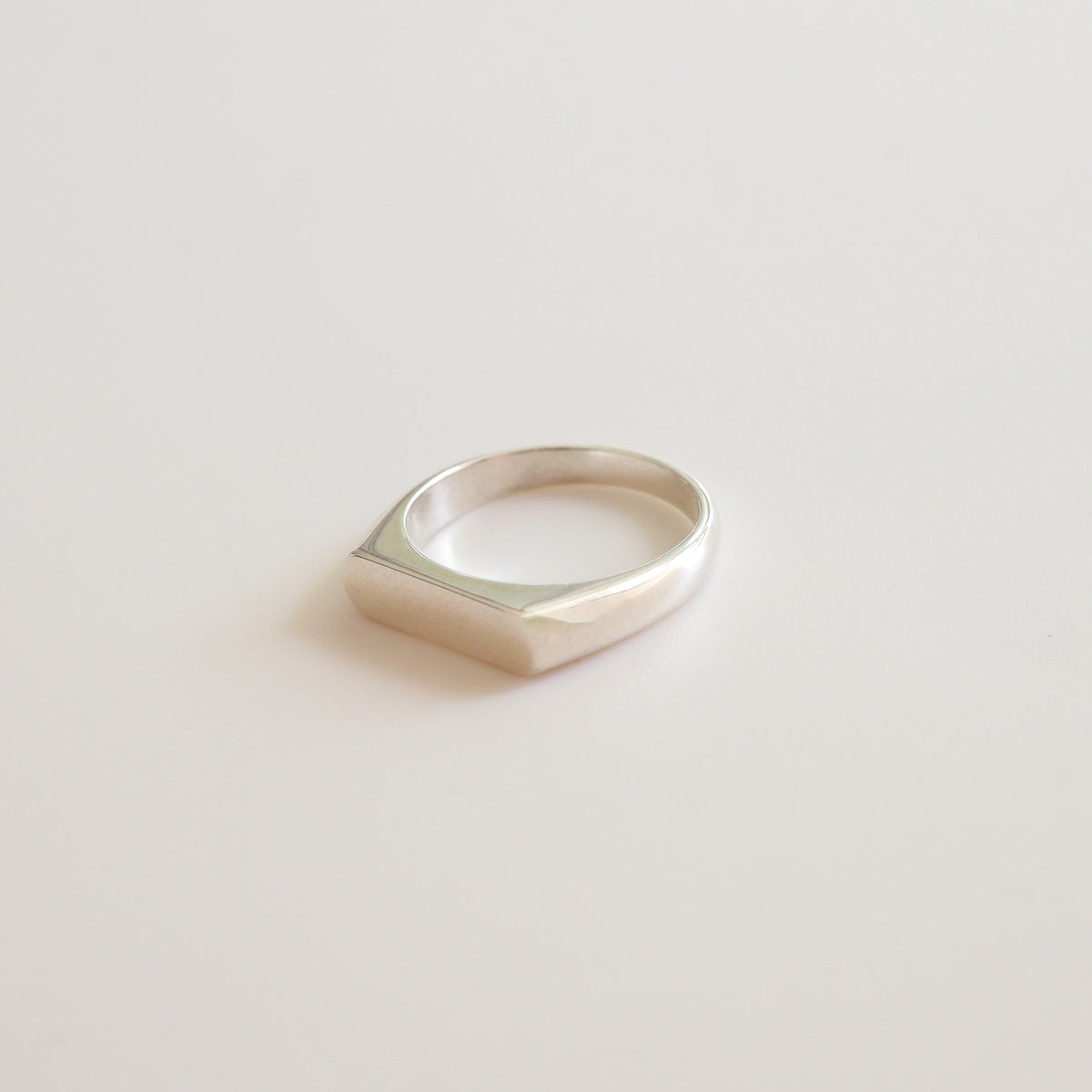 A flaylay of a narrow silver signet ring on a white background