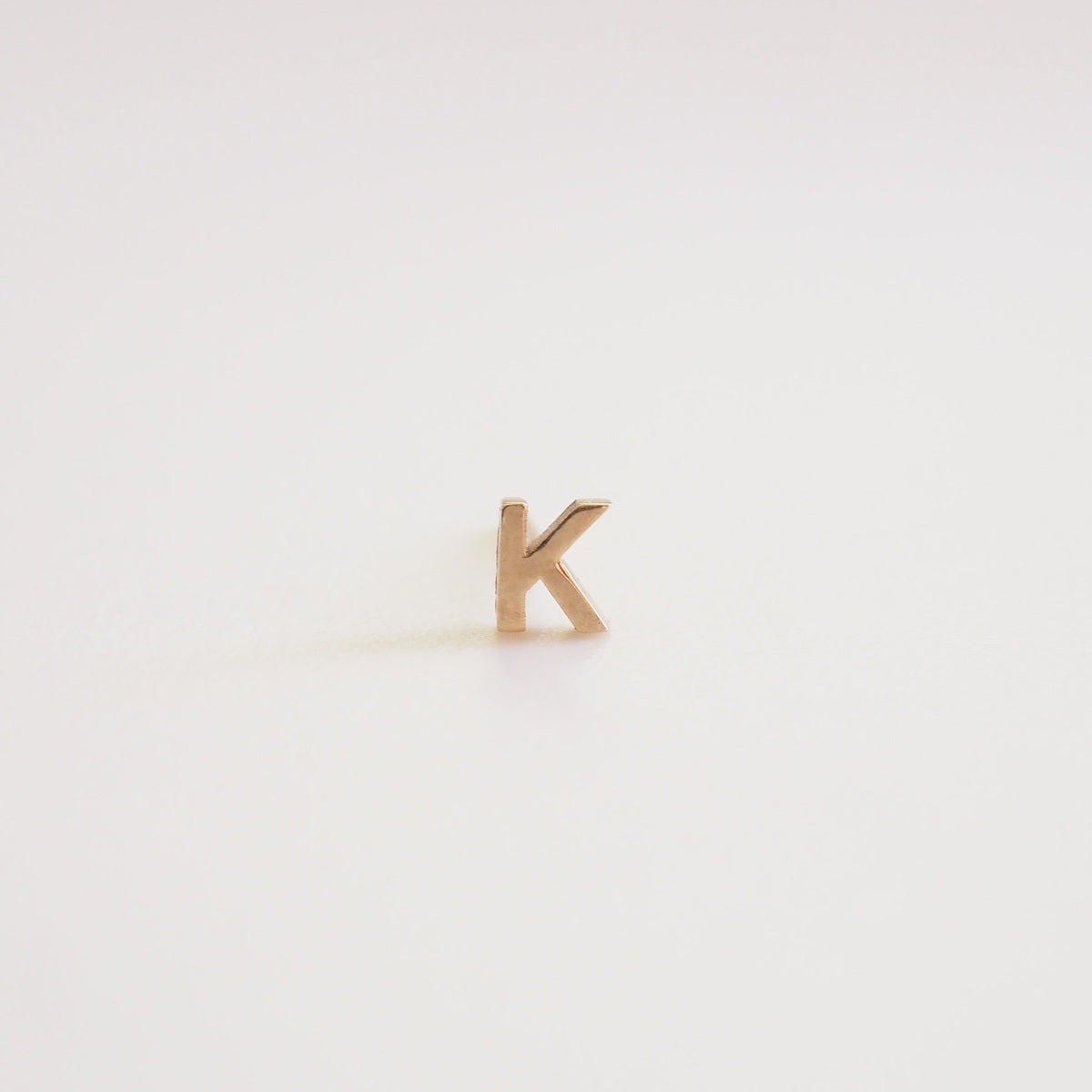 Gold letter 'K' earring on a light gray background