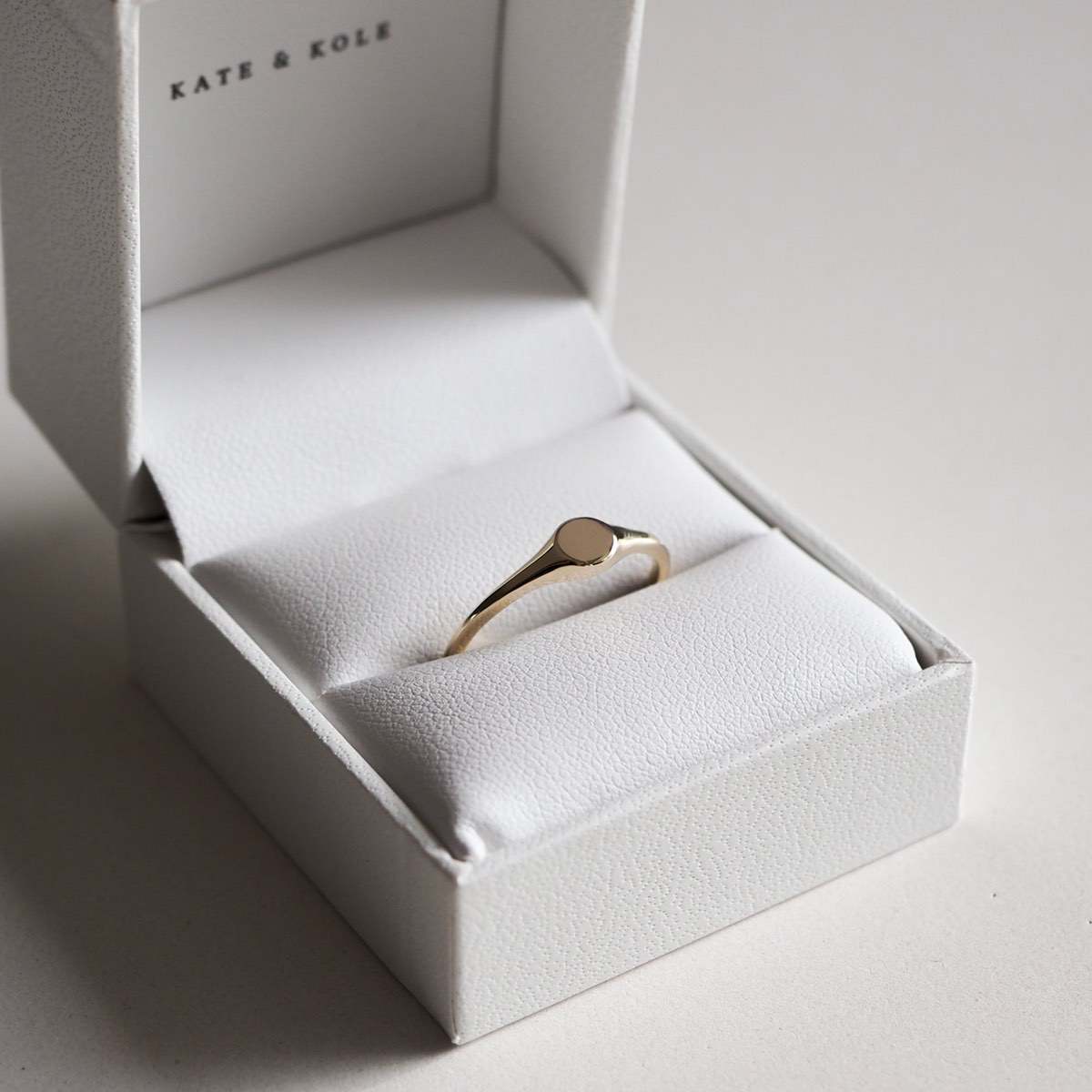 A sleek gold signet ring in an open, elegant white jewellery box from Kate & Kole, showcasing luxury and style.