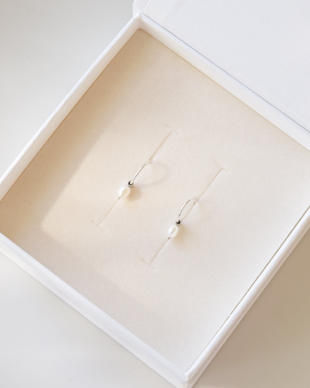 Pearl earrings in a white jewelry box on a white background