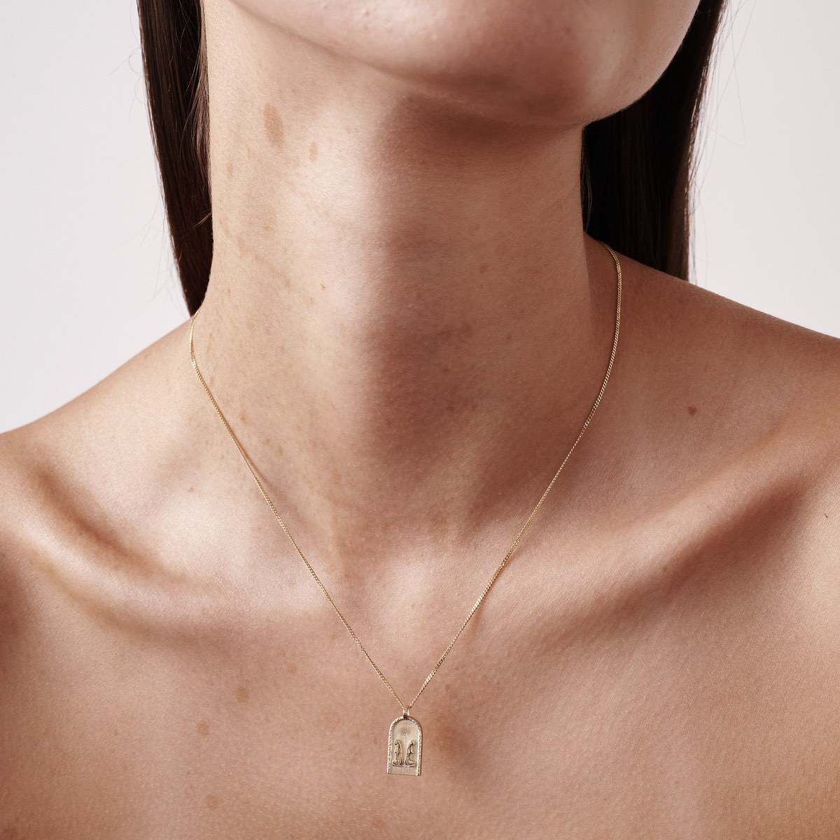 Close-up of a woman's neck wearing a delicate gold necklace with a small arch-shaped pendant; luxury jewellery showcased elegantly.