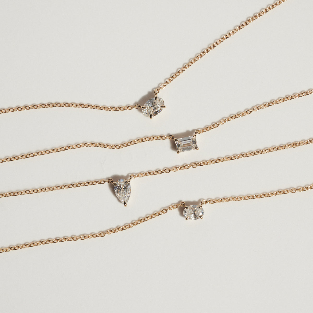 Set of gold necklaces with various diamond pendants on a light gray background