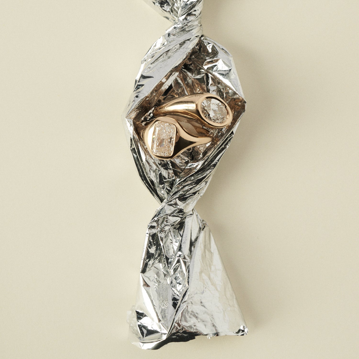 Gold ring with diamonds wrapped in clear plastic on a beige background [text overlay: 1.5ct Riva Signet]
