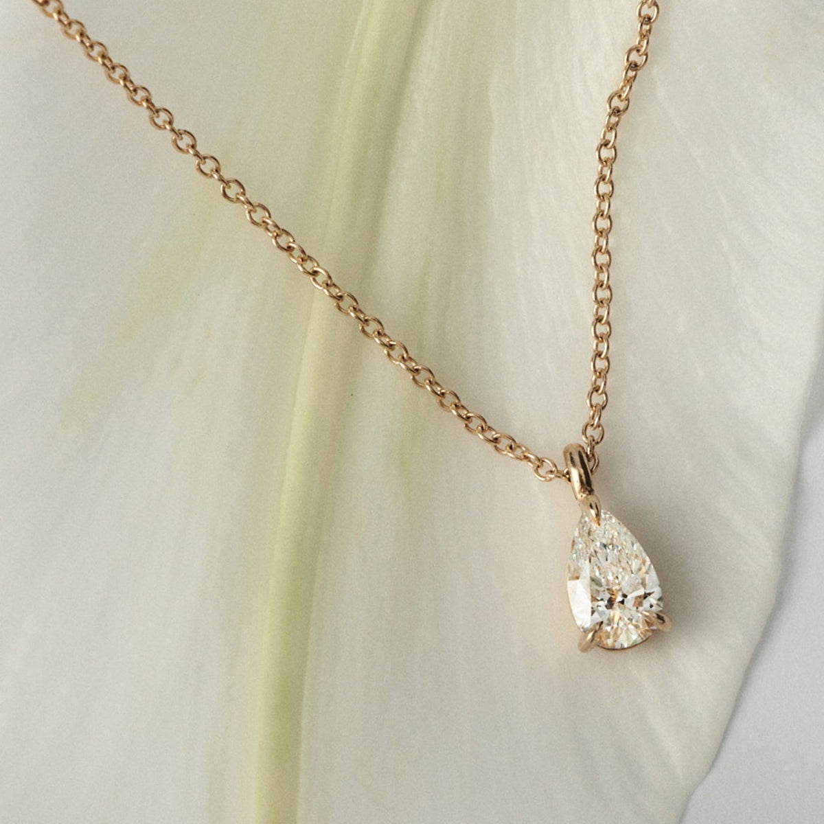 Gold necklace with a pear shaped diamond pendant on a light fabric background