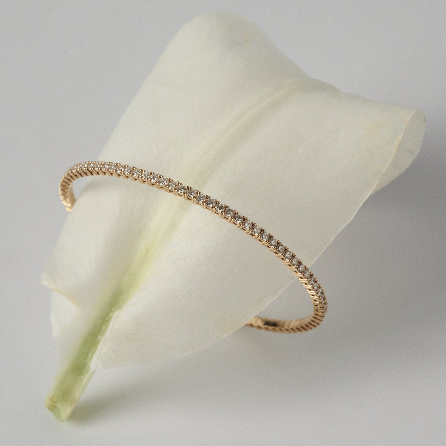 Gold bracelet with diamonds on a white petal against a light gray background