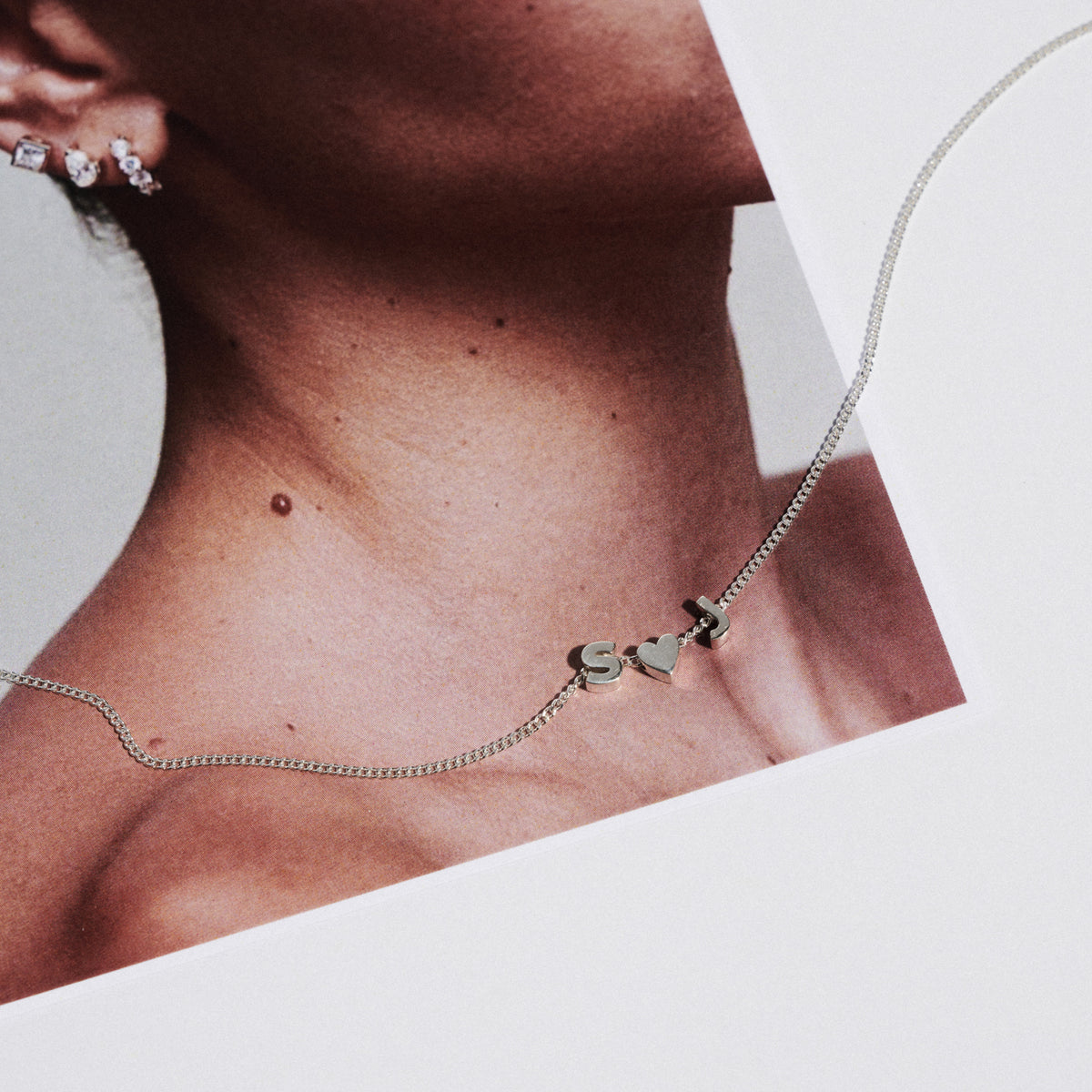 Close-up of a silver necklace with heart-shaped pendants on a neutral background [text overlay: Tiny Lovers]