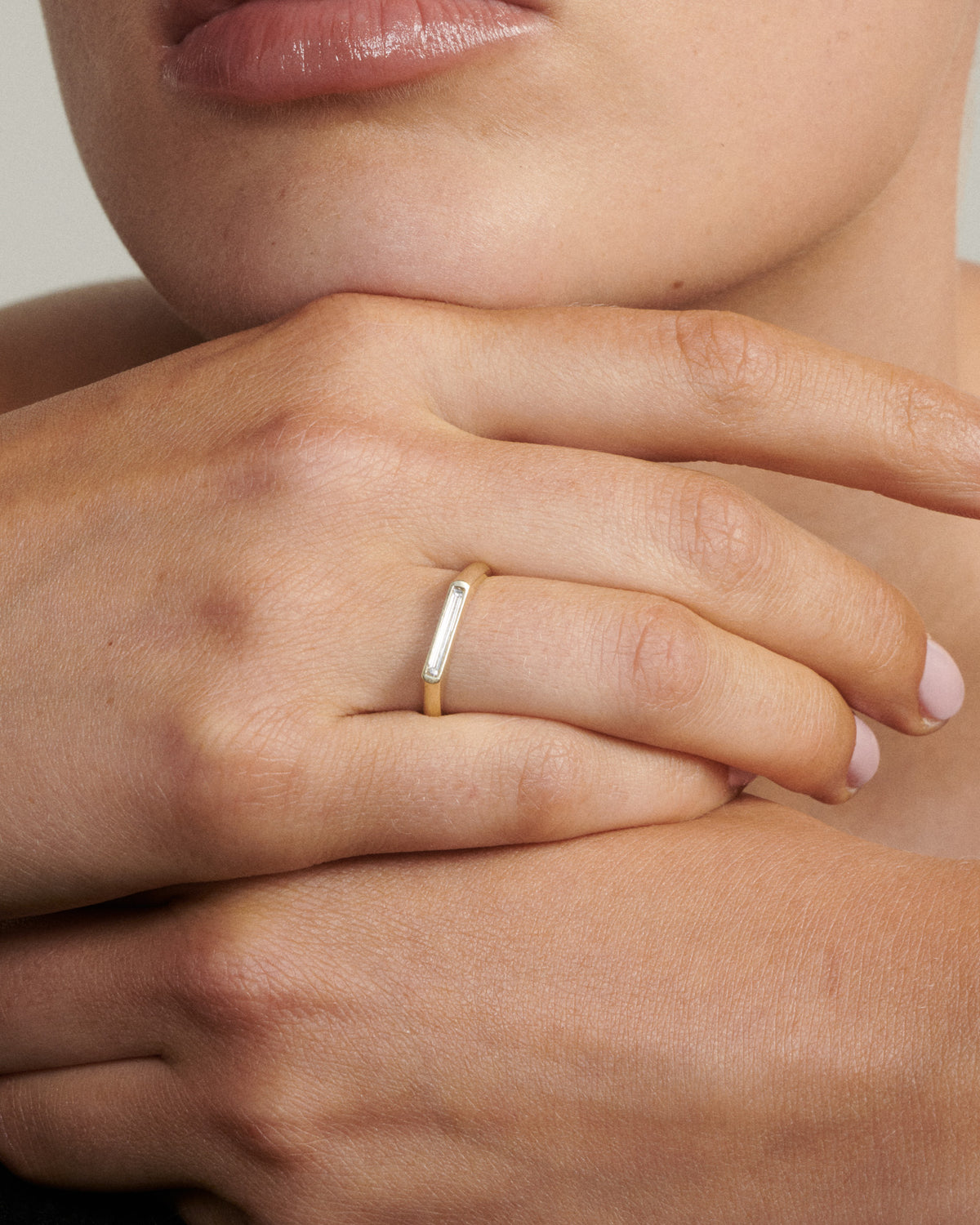 Close-up of a hand wearing a gold ring with a white stone.