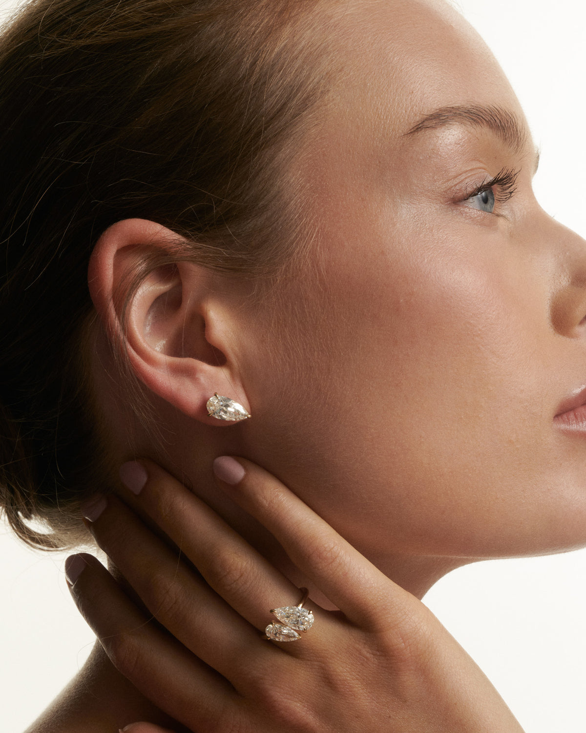 Close-up of a woman wearing diamond earrings and a ring on a neutral background
[text overlay: Andrea wears the Nouve Studs and Nouve Duet] 