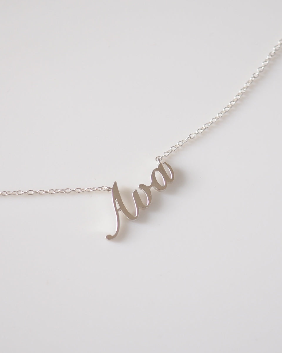 Silver necklace with 'Ava' pendant on a light gray background
