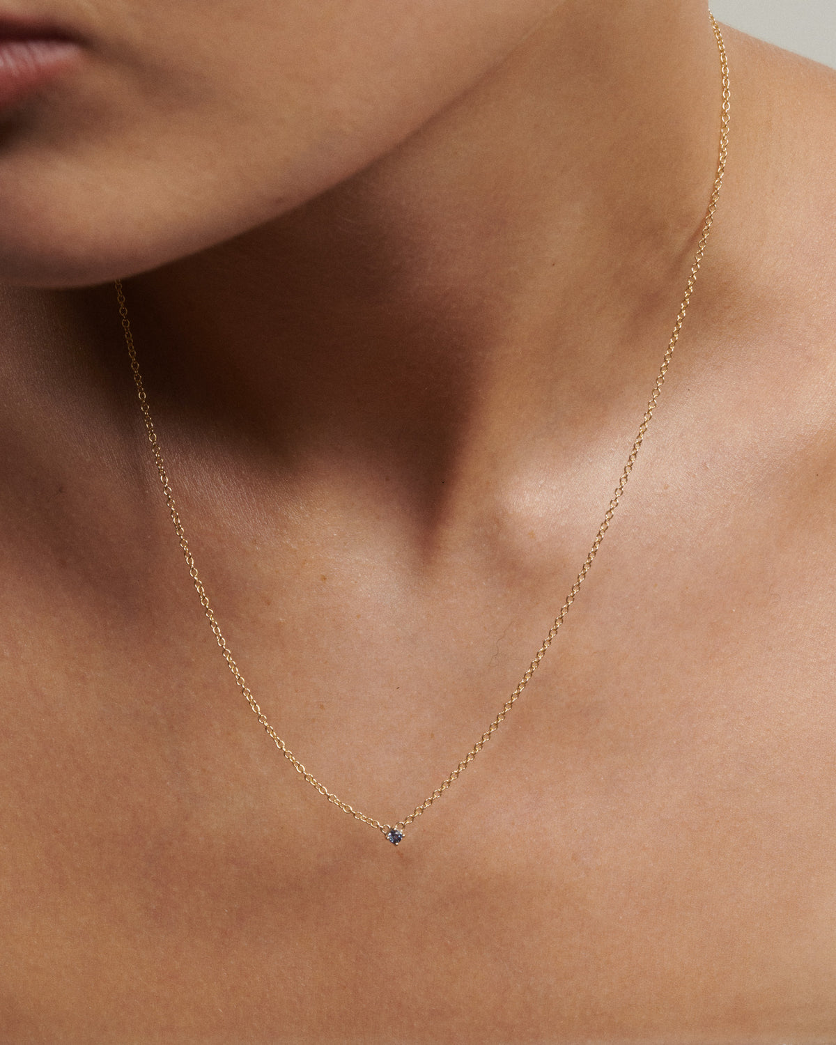 Gold necklace with a small blue gemstone on a person's neck