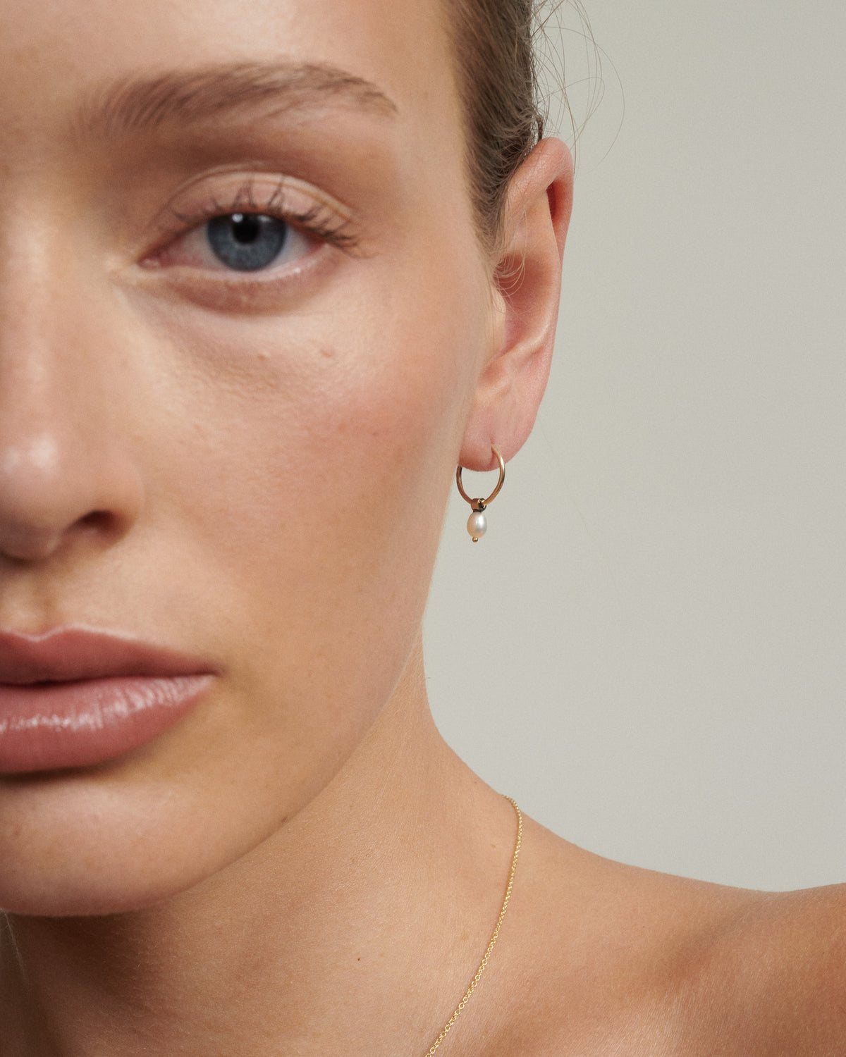 Close-up of a person wearing a gold hoop earring with a neutral background