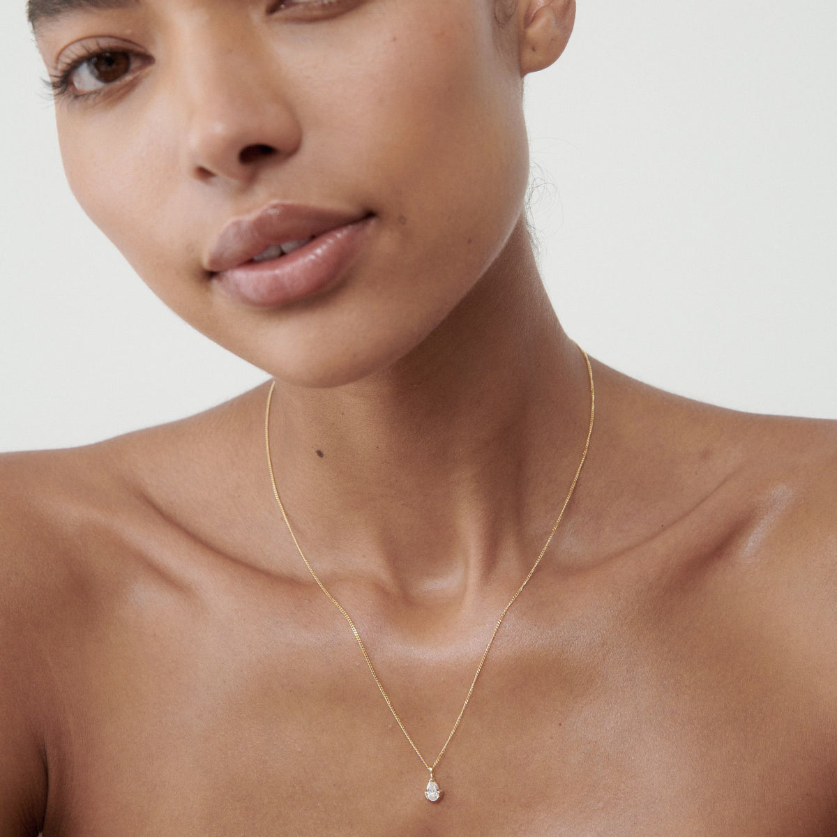 Woman wearing a delicate gold necklace with a small pearl pendant, shown against a soft background, exuding luxury and elegance.