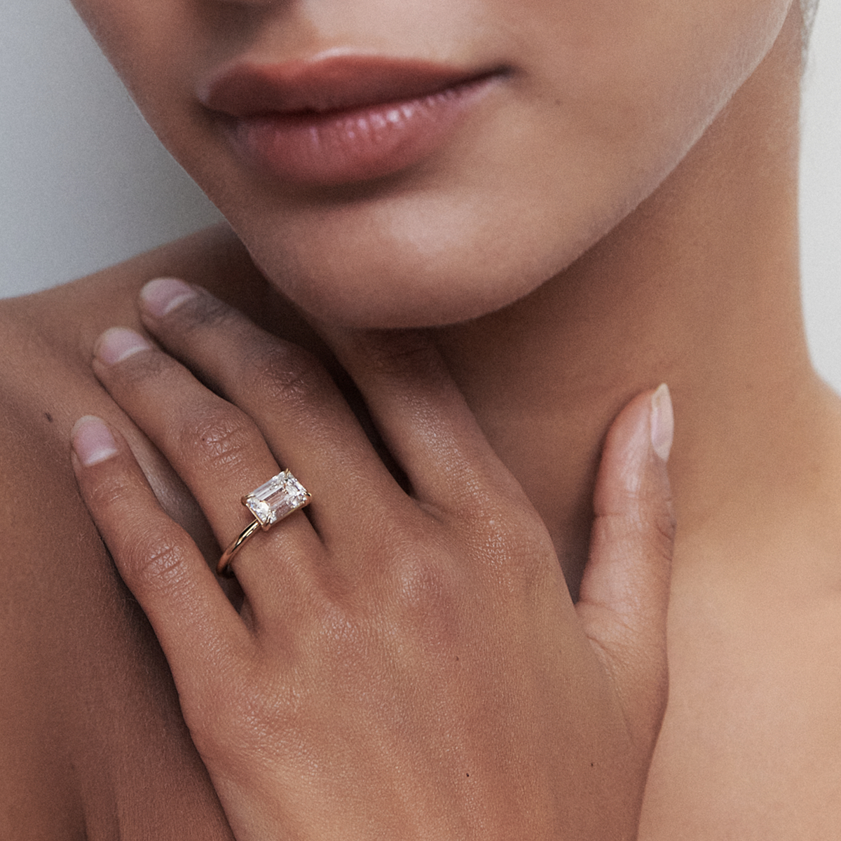 Close-up of a woman wearing an emerald-cut diamond ring on her finger, highlighting luxury jewellery with a gold band.