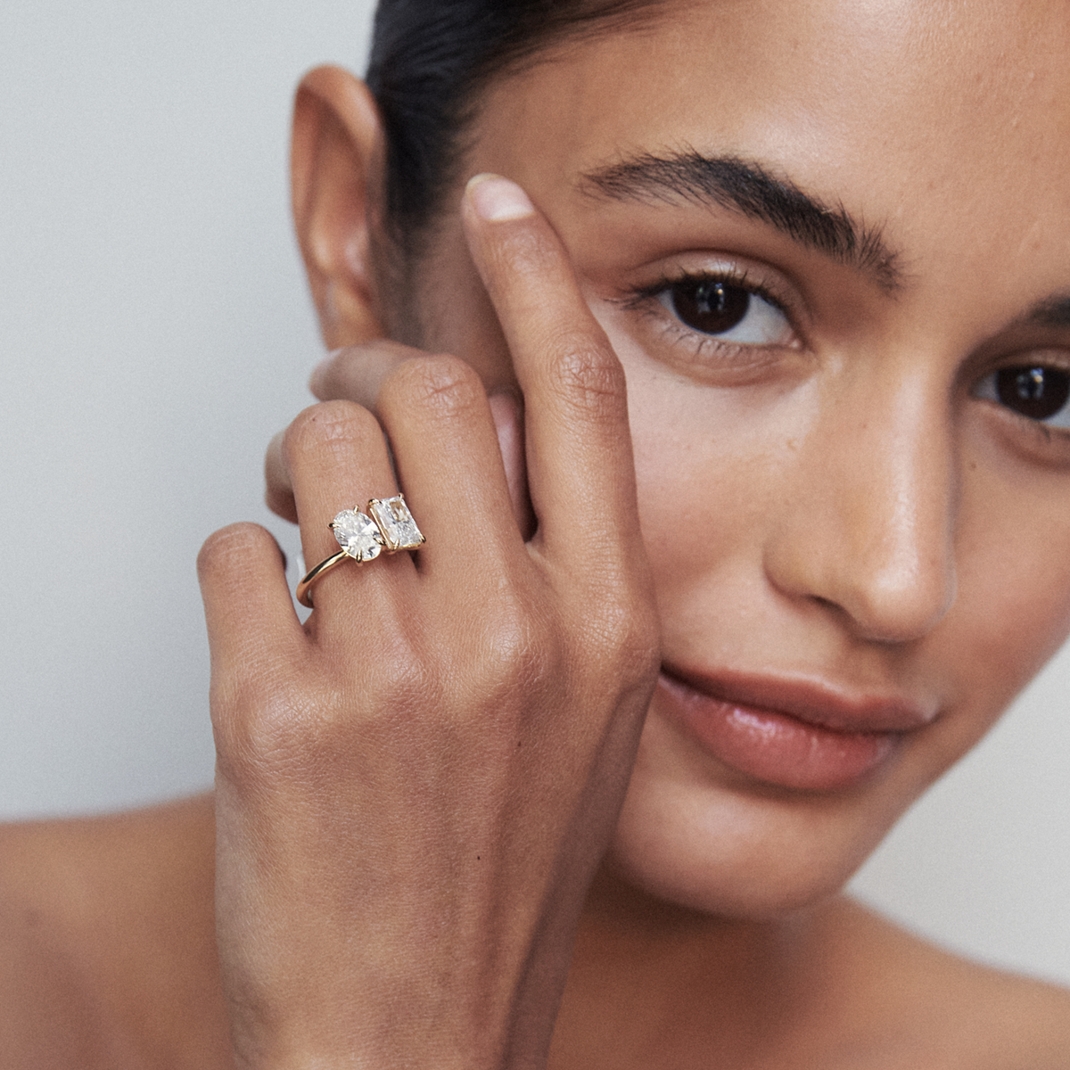 Woman wearing a dual-stone gold ring with large gemstones against her cheek. Luxury jewellery, elegant style.