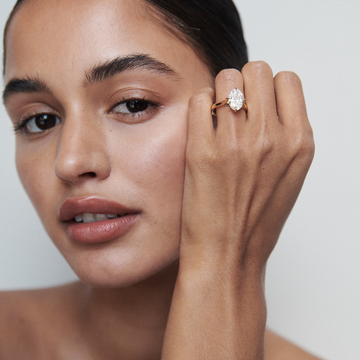 Woman showcasing a gold ring with an oval diamond. Minimalist background highlights luxury jewellery elegance. Australia style beauty.