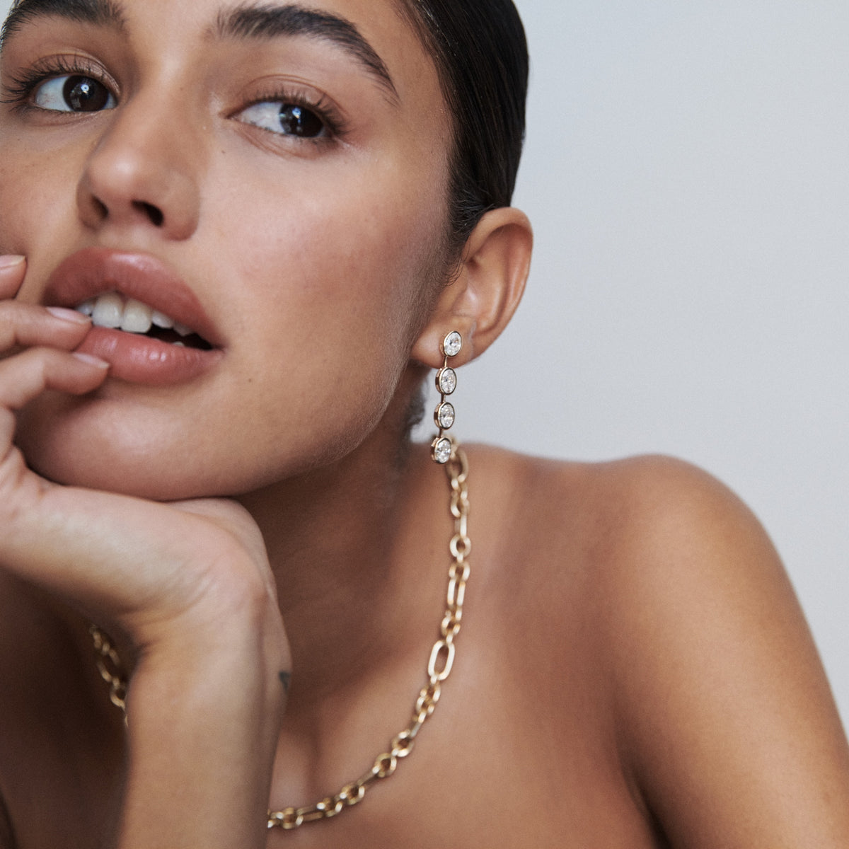 Woman wearing elegant diamond drop earrings and a chunky gold chain necklace, gazing to the side. Luxe jewellery, minimalist style.