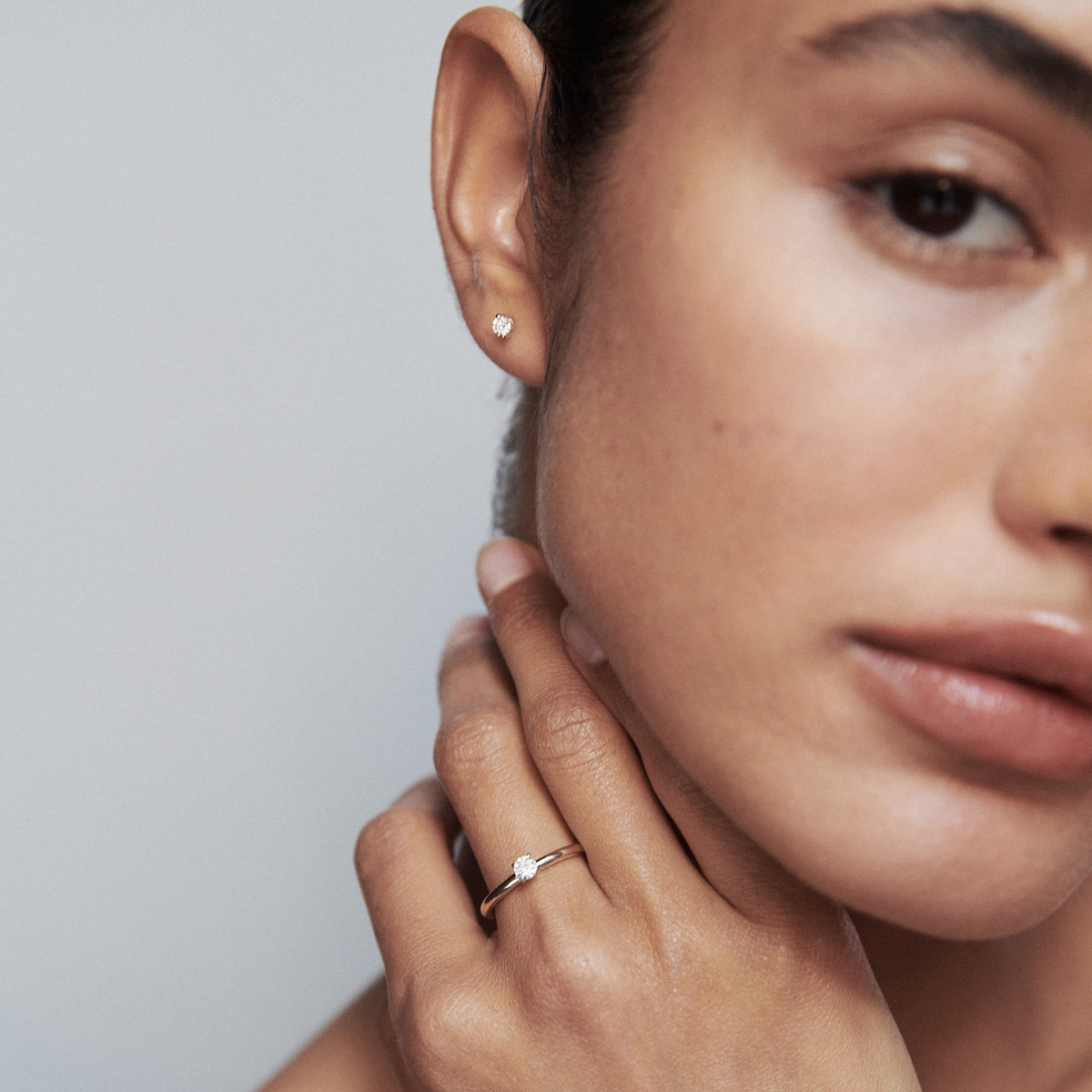 Close-up of a woman's face, focusing on a gold hoop earring and delicate ring with a diamond. Perfect for luxury jewellery marketing.