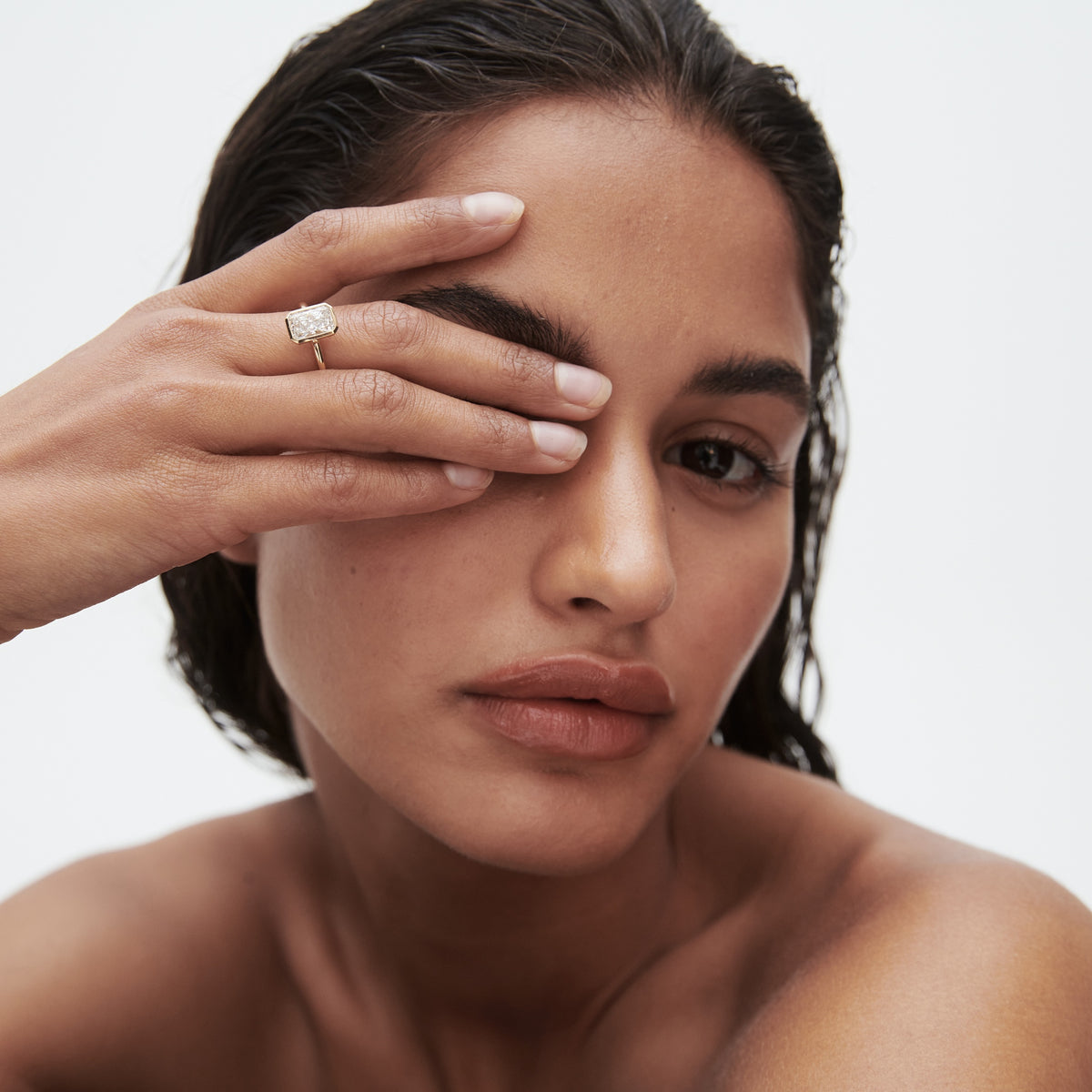 Woman showcases a luxury ring, partially covering face with her hand; minimalist, high-end jewellery portrait.