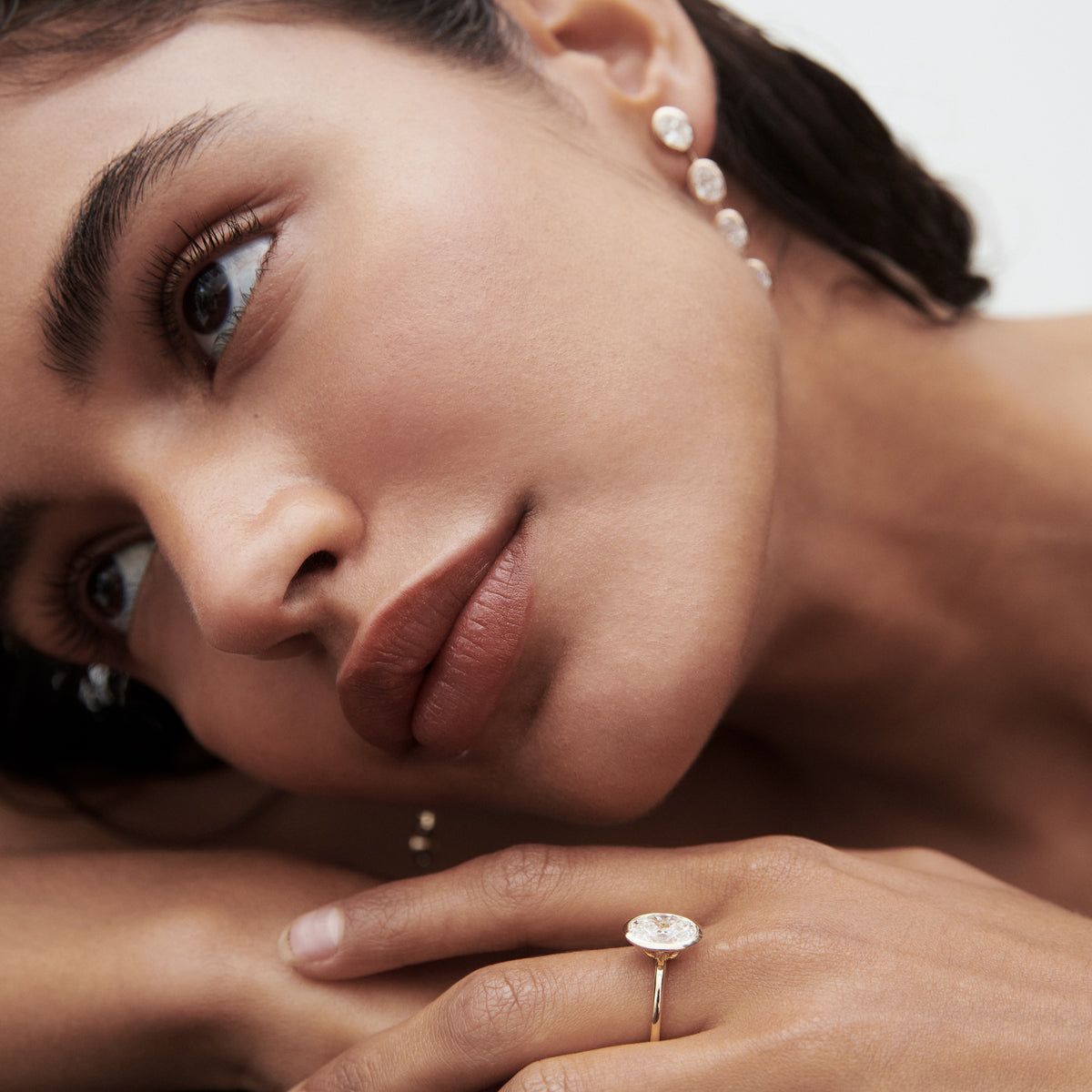 Woman with elegant jewelry; wearing an oval diamond ring and a cascading pearl earring. Sophisticated and luxurious style.