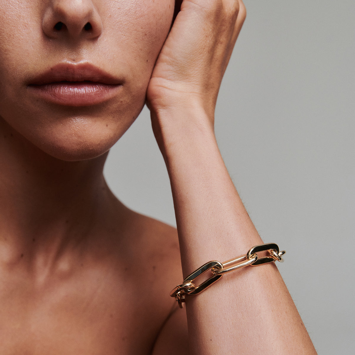 Close-up of a person wearing a gold chain bracelet on a neutral background