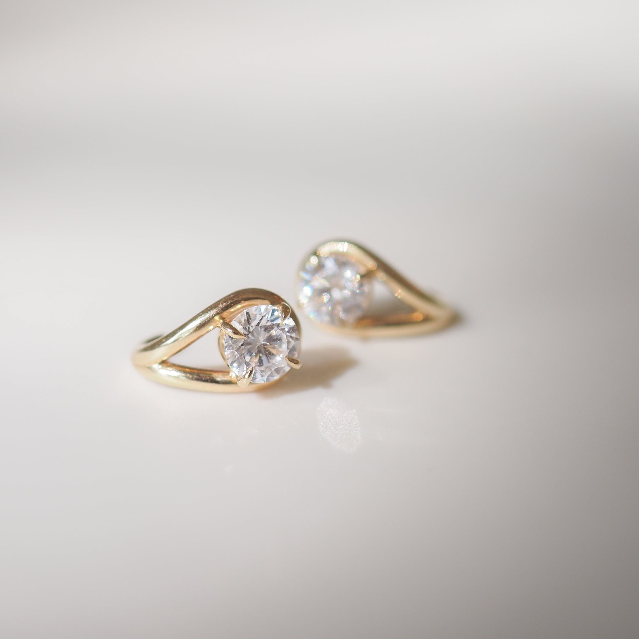 Gold earrings with round diamonds on a light surface, showcasing luxury jewellery design and elegance.