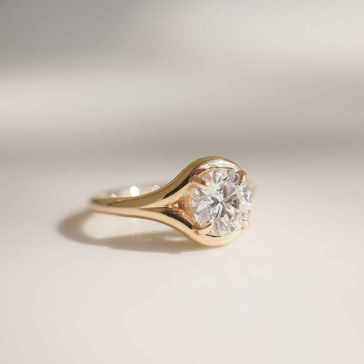 Gold ring with a large, round-cut diamond solitaire, elegantly set in a polished band, casting a subtle shadow on a light surface.
