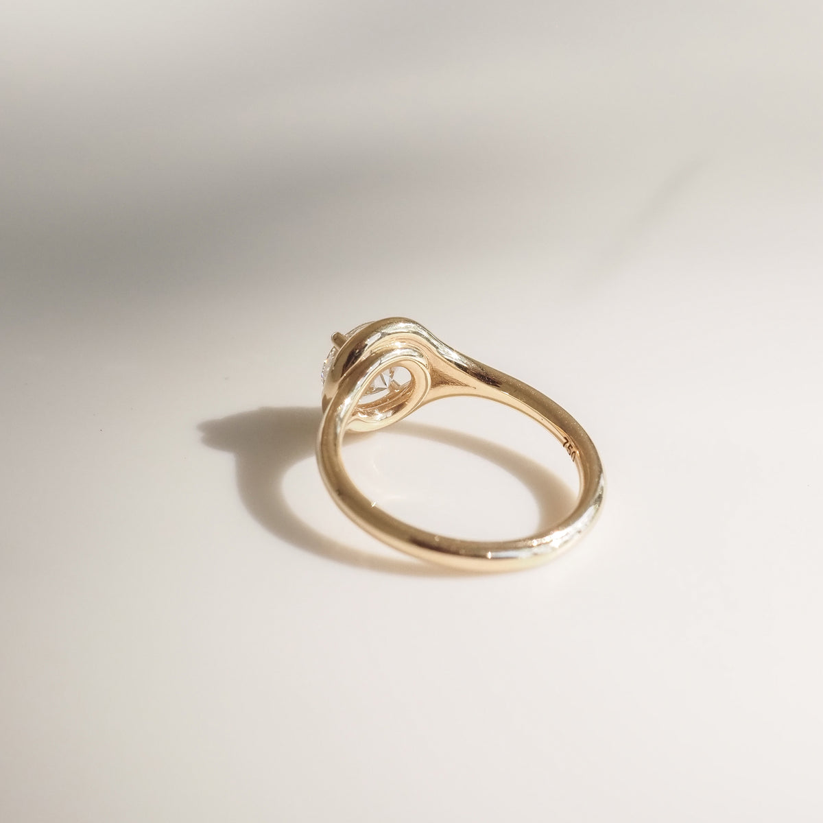 Elegant gold ring with a unique, twisted band design, set with a solitaire diamond, casting a soft shadow on a smooth surface.