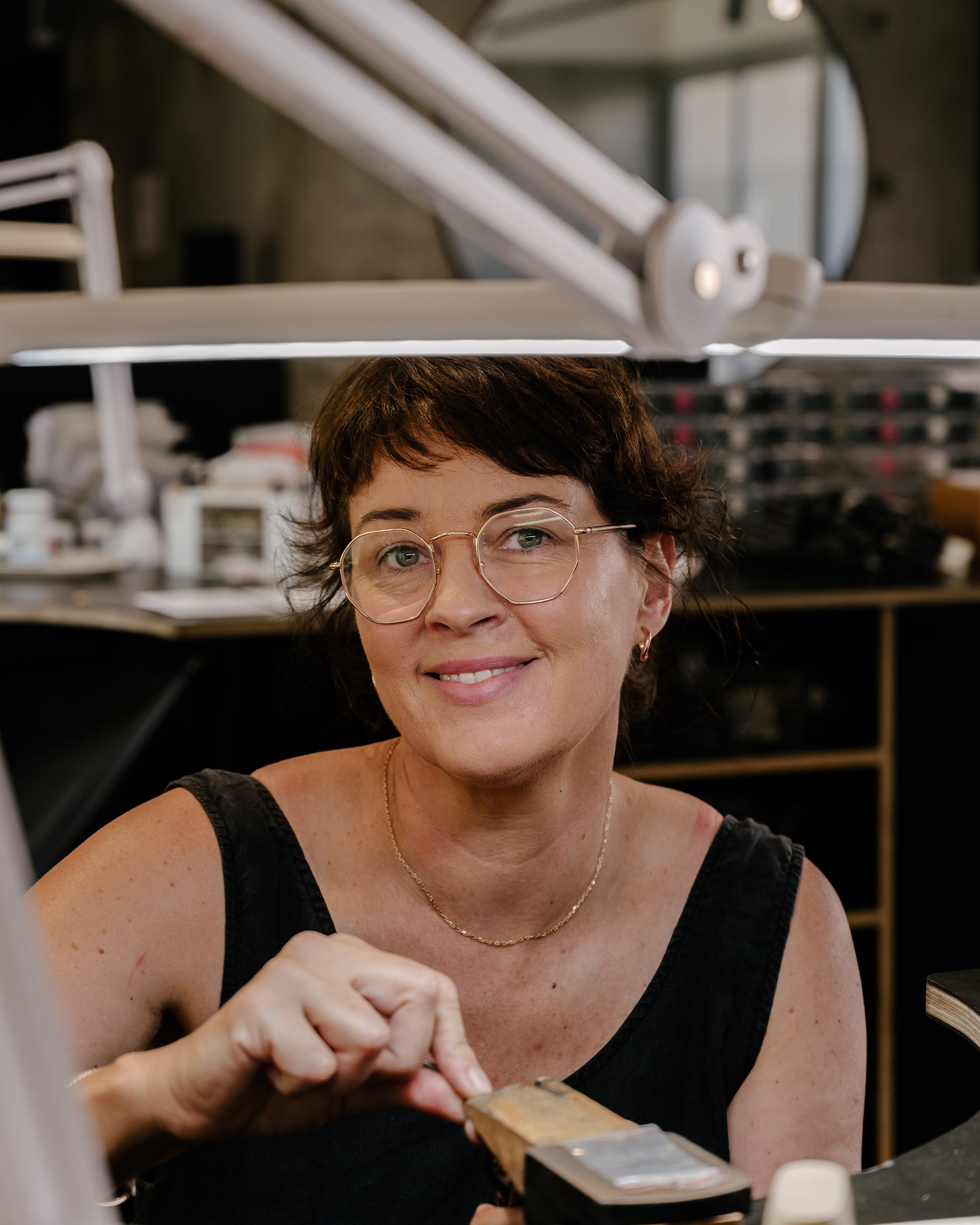 Jeweller crafting luxury jewellery in studio, smiling, tools visible. Elegant, high-end aesthetic.