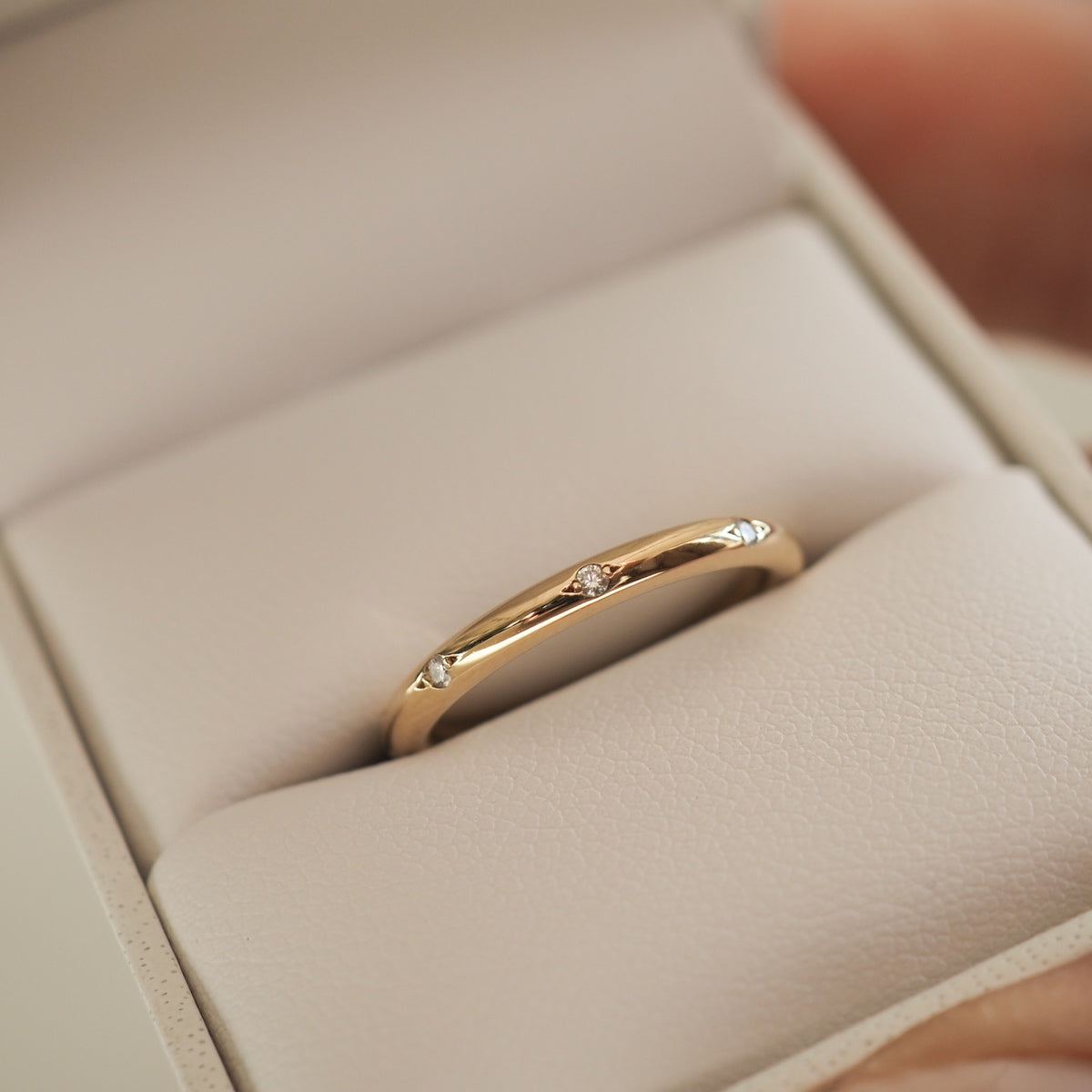 Gold ring with small diamonds, elegantly displayed in a cream-coloured jewellery box.